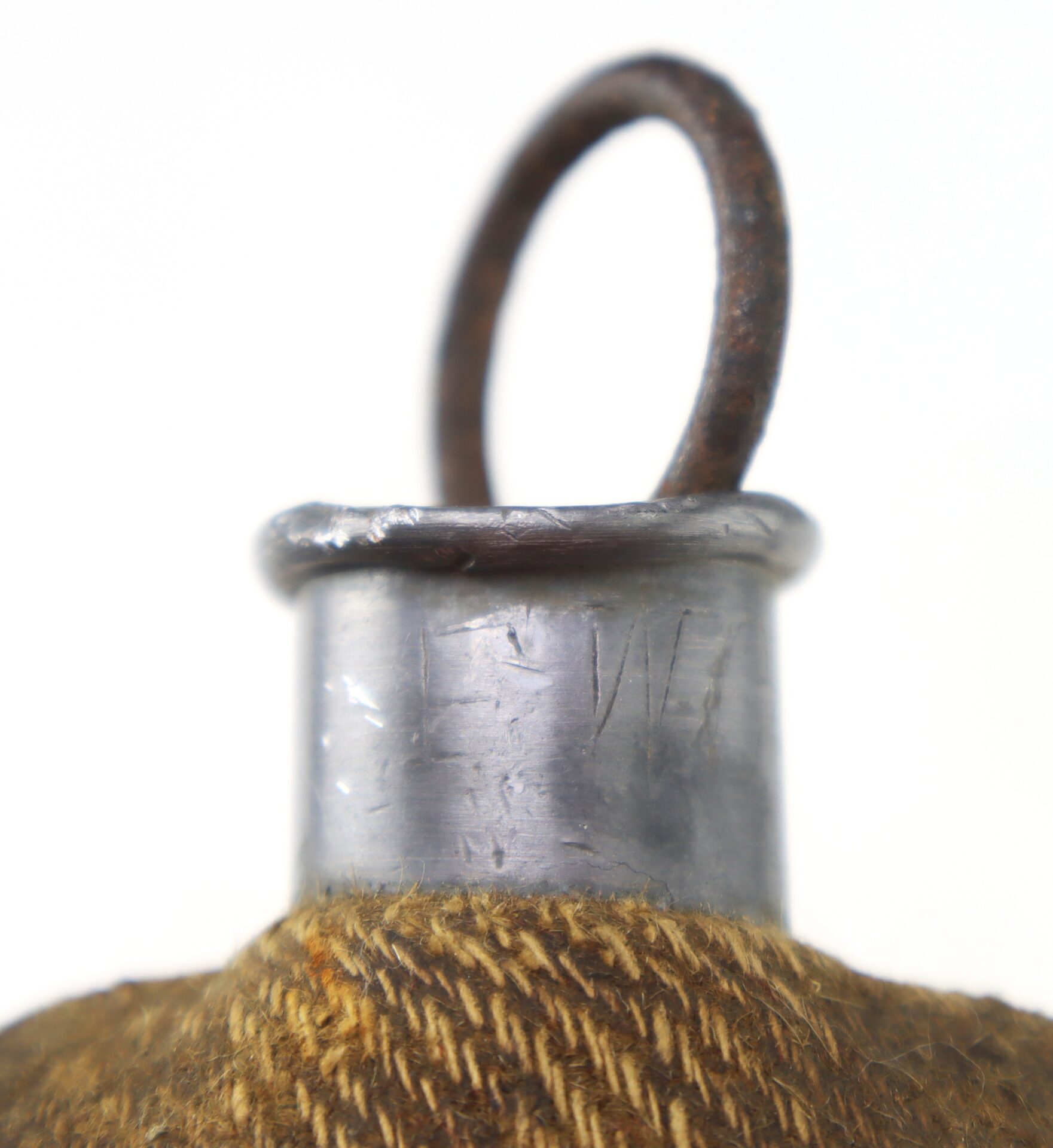Close-up of a metal canteen neck with a rusted loop and a brown textured fabric covering the body; letters are faintly engraved on the metal.