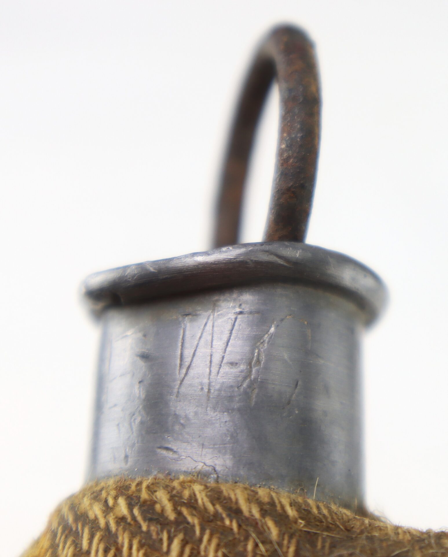Close-up of a metal object with a circular loop on top and the letters "W C" etched on the surface, partially wrapped in a coarse fabric.