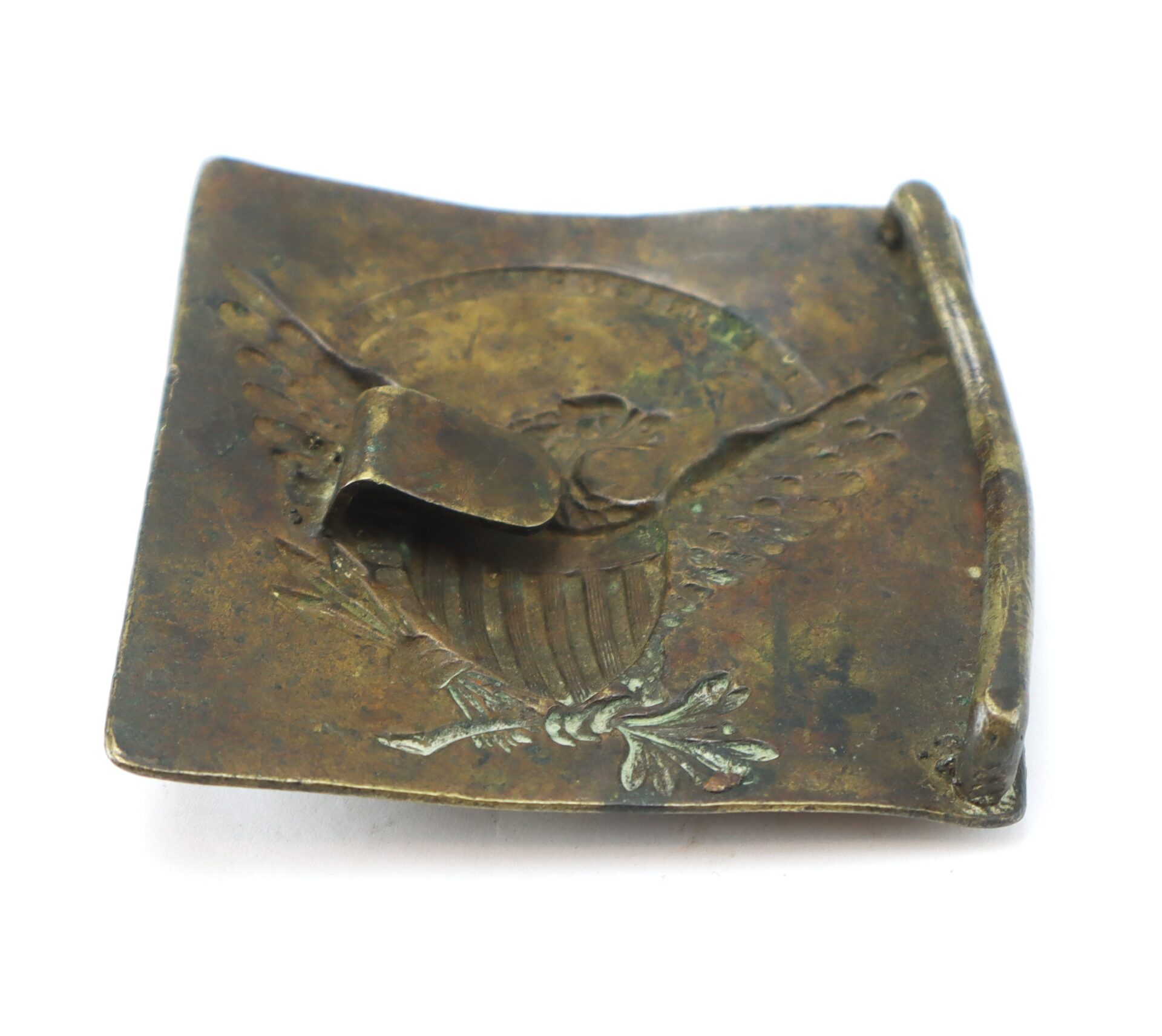 Square brass plate with a raised Great Seal of the United States, featuring an eagle, arrows, and olive branch; includes a bent attachment hook on the back.