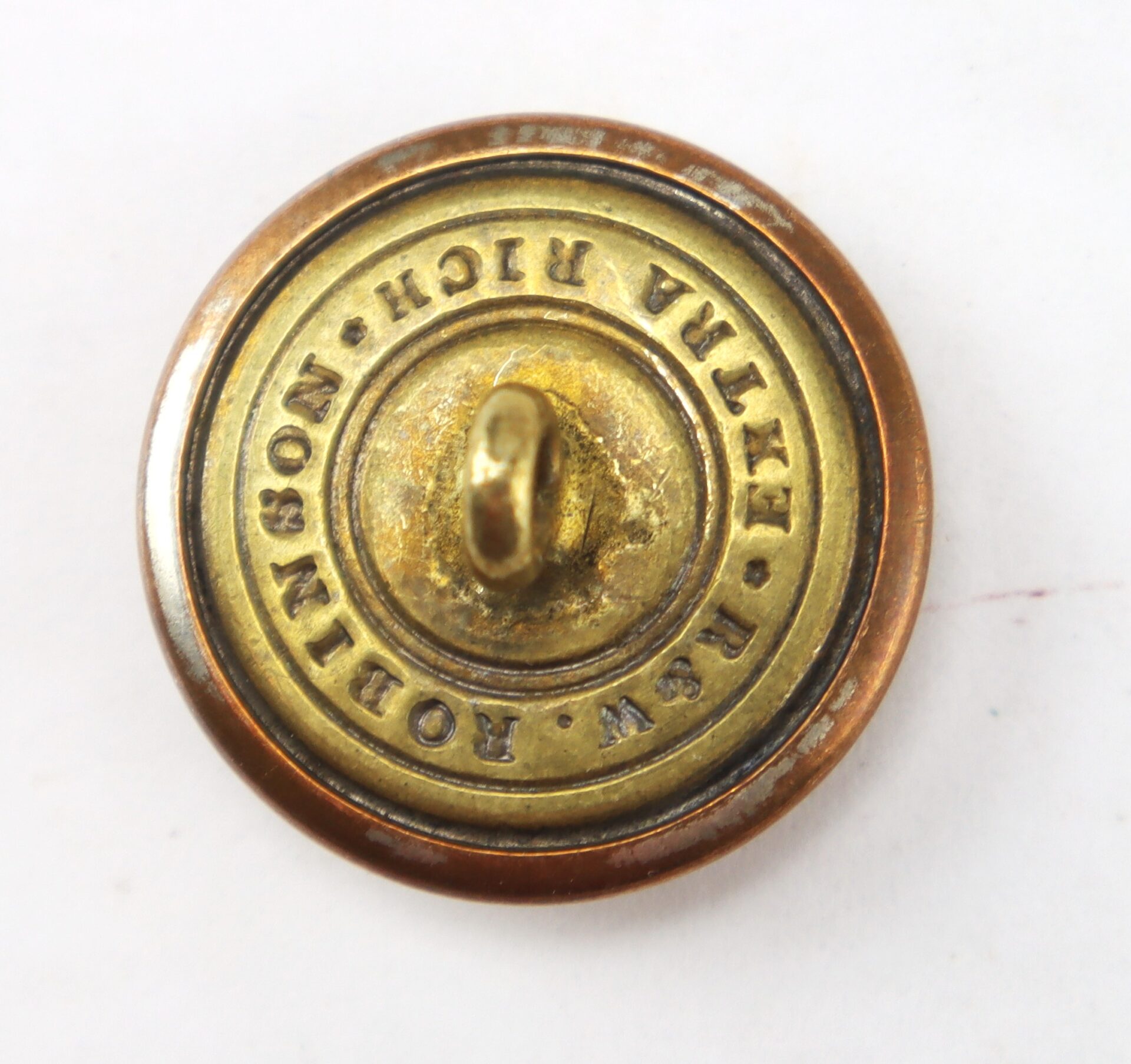 A round brass button with a central shank, inscribed “J.W. Robinson, Extra Rich” around the edge, photographed against a white background.