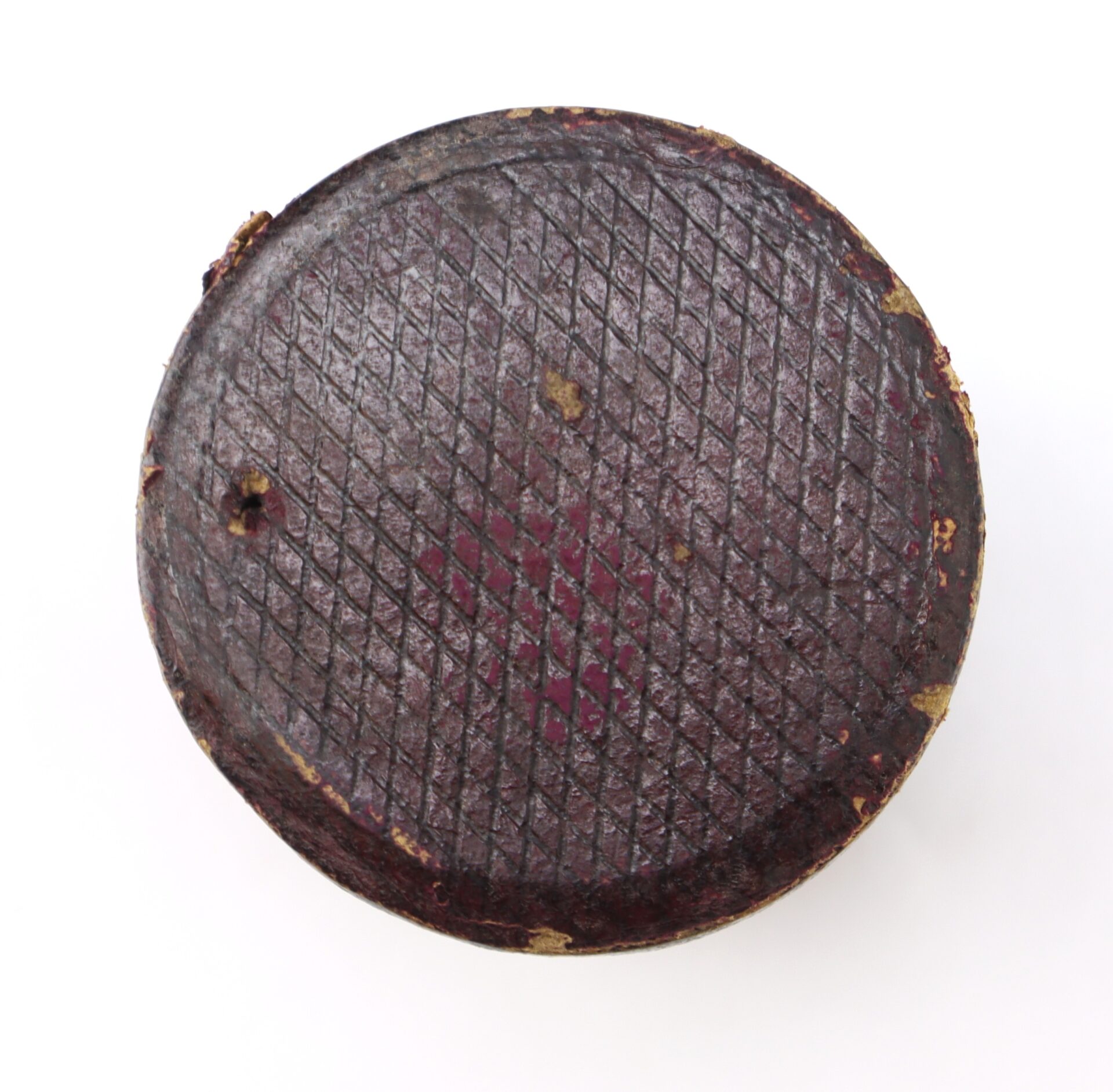 A round, dark brown object with a textured, crosshatched surface and some worn edges, viewed from above on a white background.