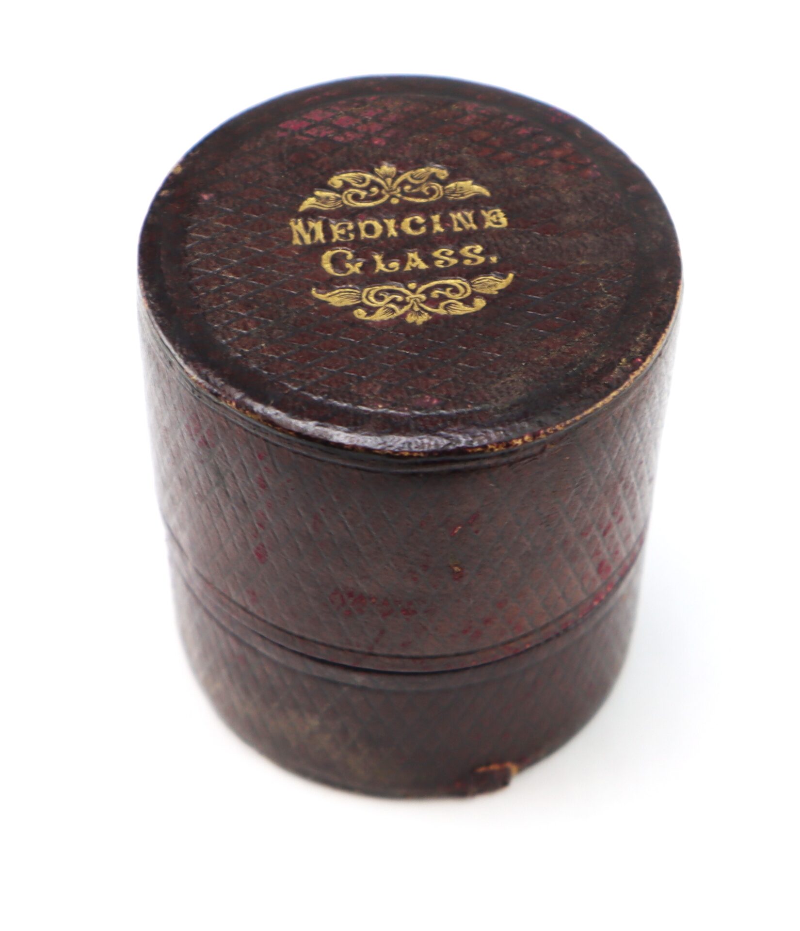 A round, brown leather case with the words "Medicine Glass" printed in gold on the lid, shown against a white background.