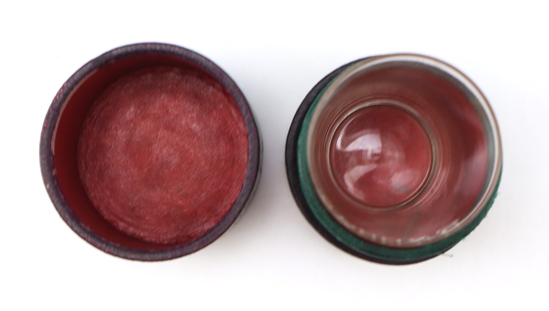 A small, round, empty container with a red interior is shown next to its matching glass lid, both placed on a white background.