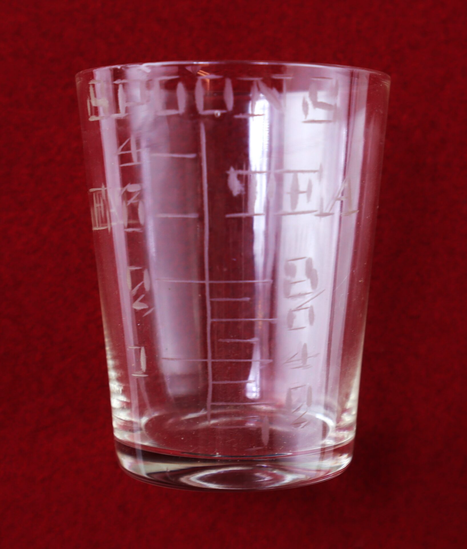 A clear glass measuring cup with etched measurement markings, placed against a red background.