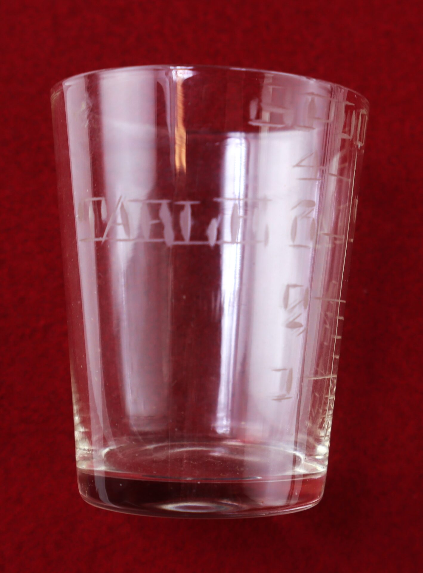 A clear glass measuring cup with etched markings, placed against a red background.