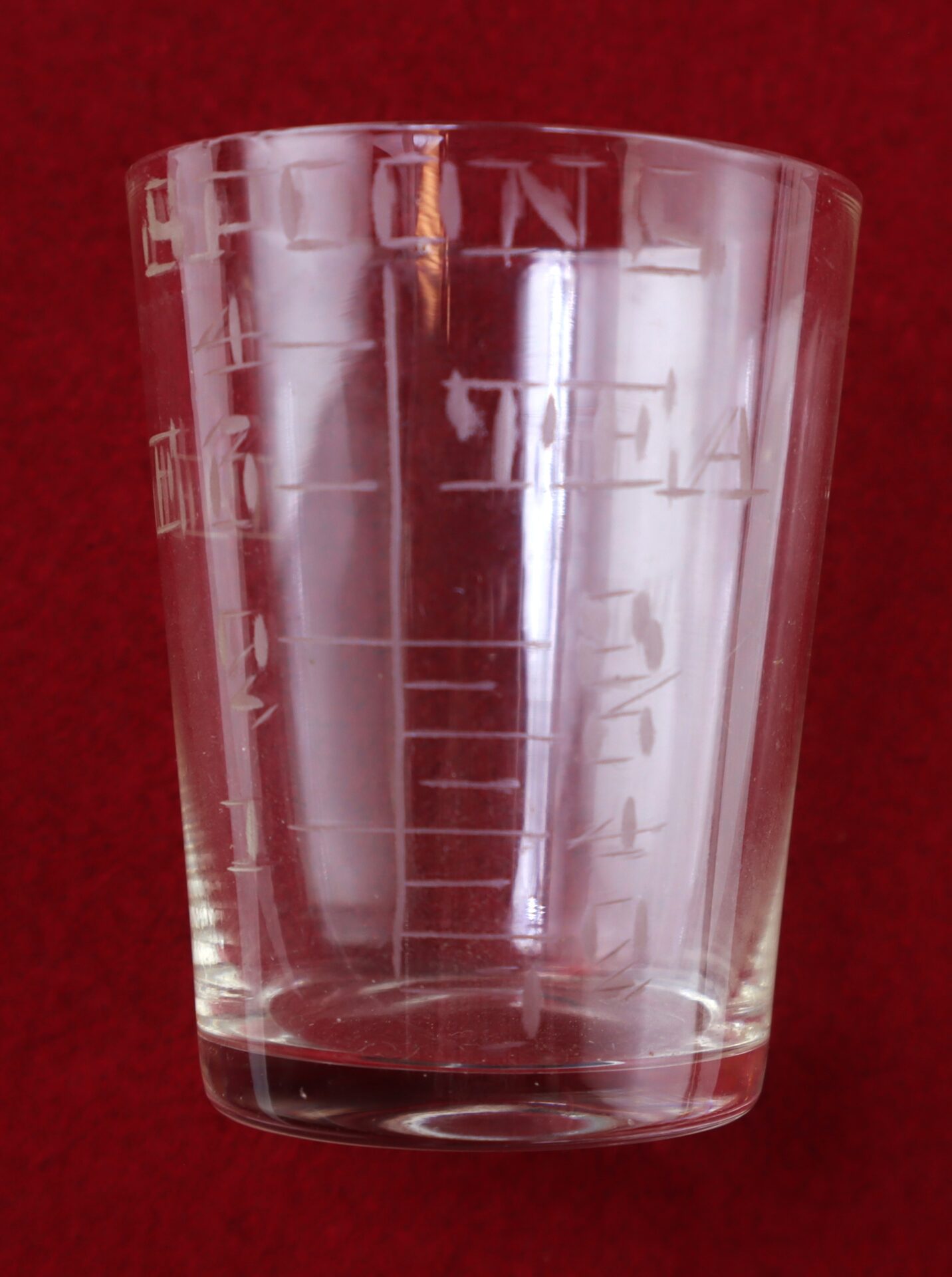 A glass measuring cup with etched markings for measurements, set against a red background.