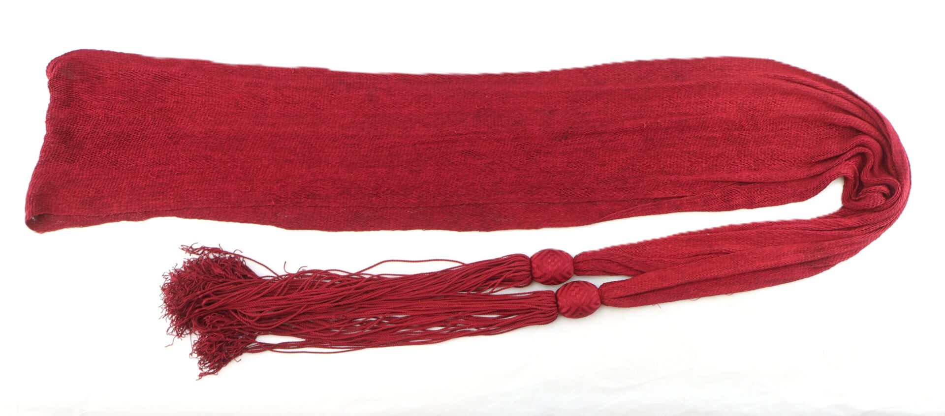A long, red woven sash with two large tassels at one end, displayed on a white background.