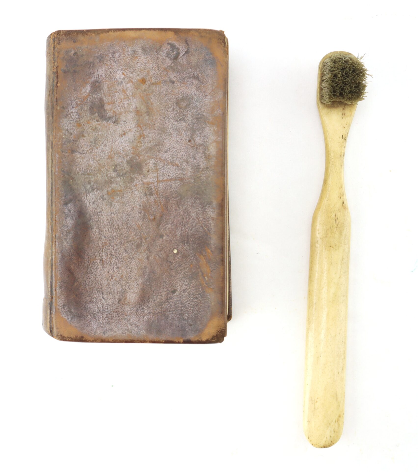 A Confederate Bible with a worn brown leather cover sits beside a wooden toothbrush with dark bristles on a white background.