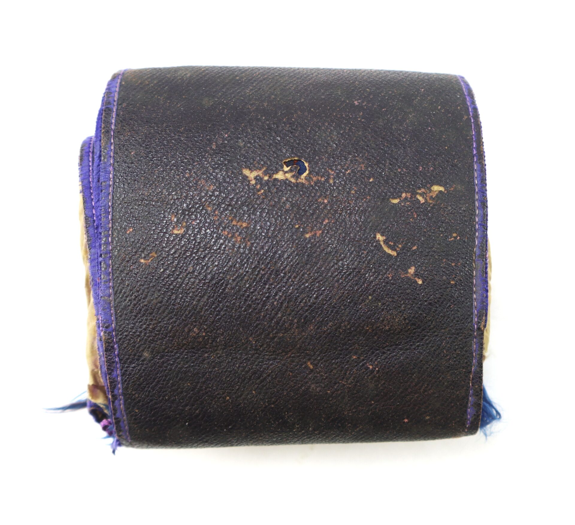 Worn, rectangular object wrapped in dark leather with visible hole in the center and purple-edged fabric trim, photographed against a white background.