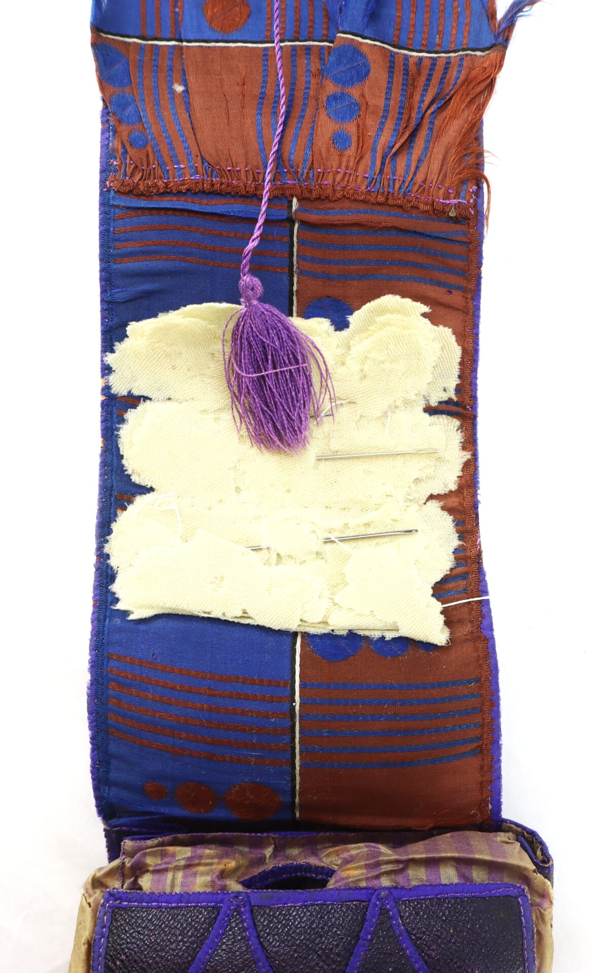 A close-up of a decorative textile with geometric blue and brown patterns, a frayed cream-colored patch, and a purple tassel.