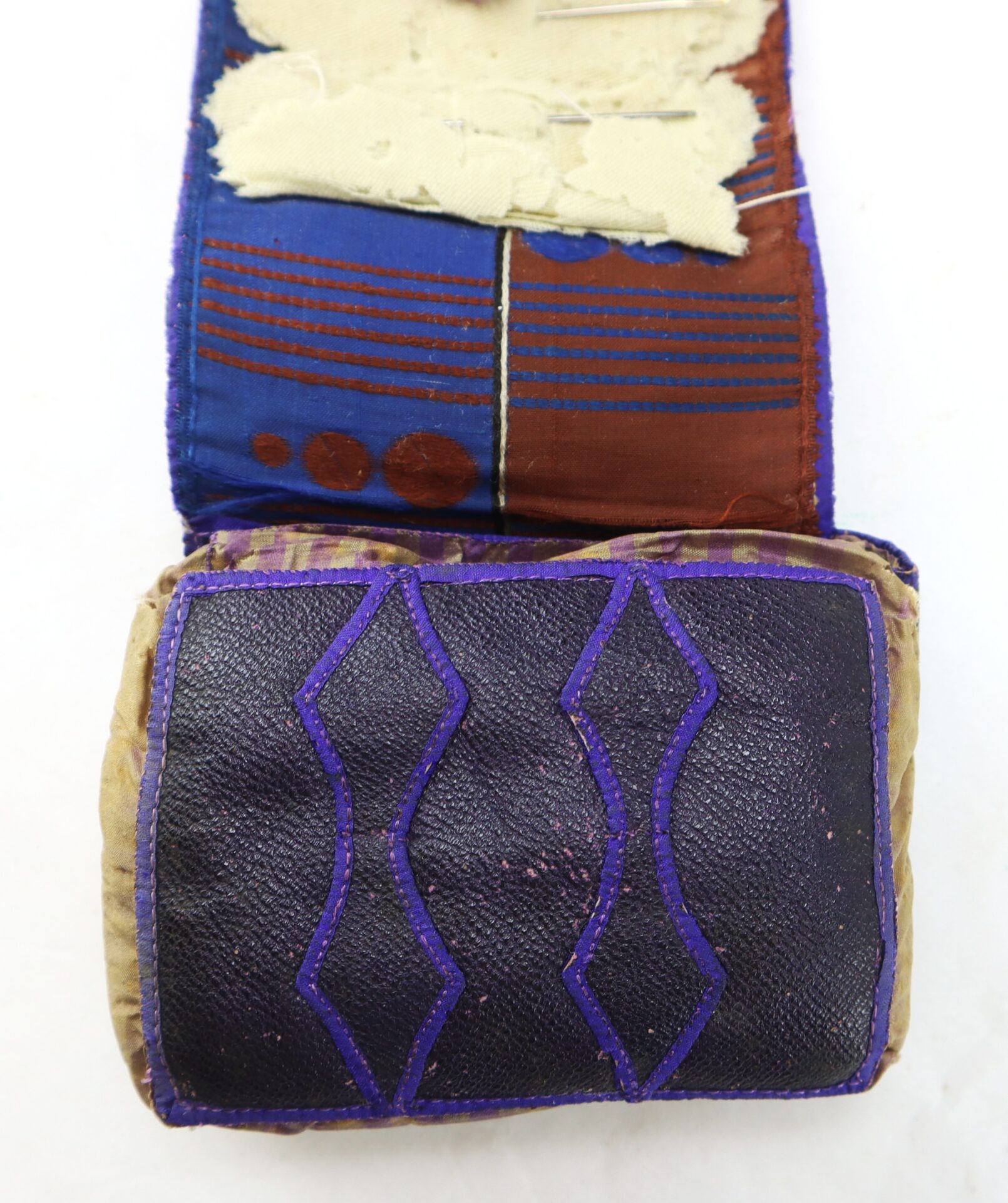 A rectangular fabric pouch with a flap, featuring dark and light fabrics, geometric stitched patterns, and some worn or frayed areas.