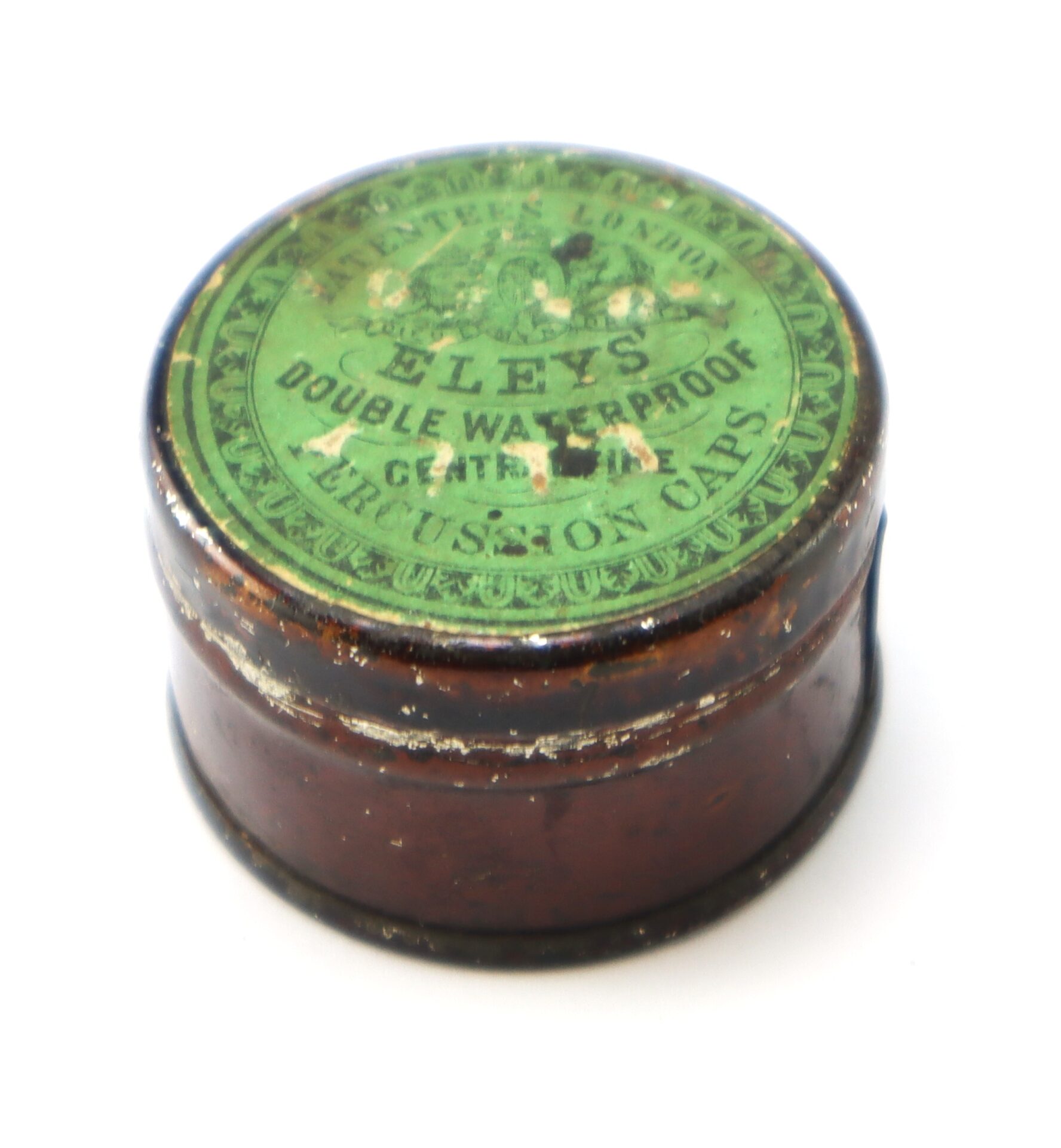A round, brown metal tin with a worn green label reading "Eley's Double Waterproof Central Fire Percussion Caps.