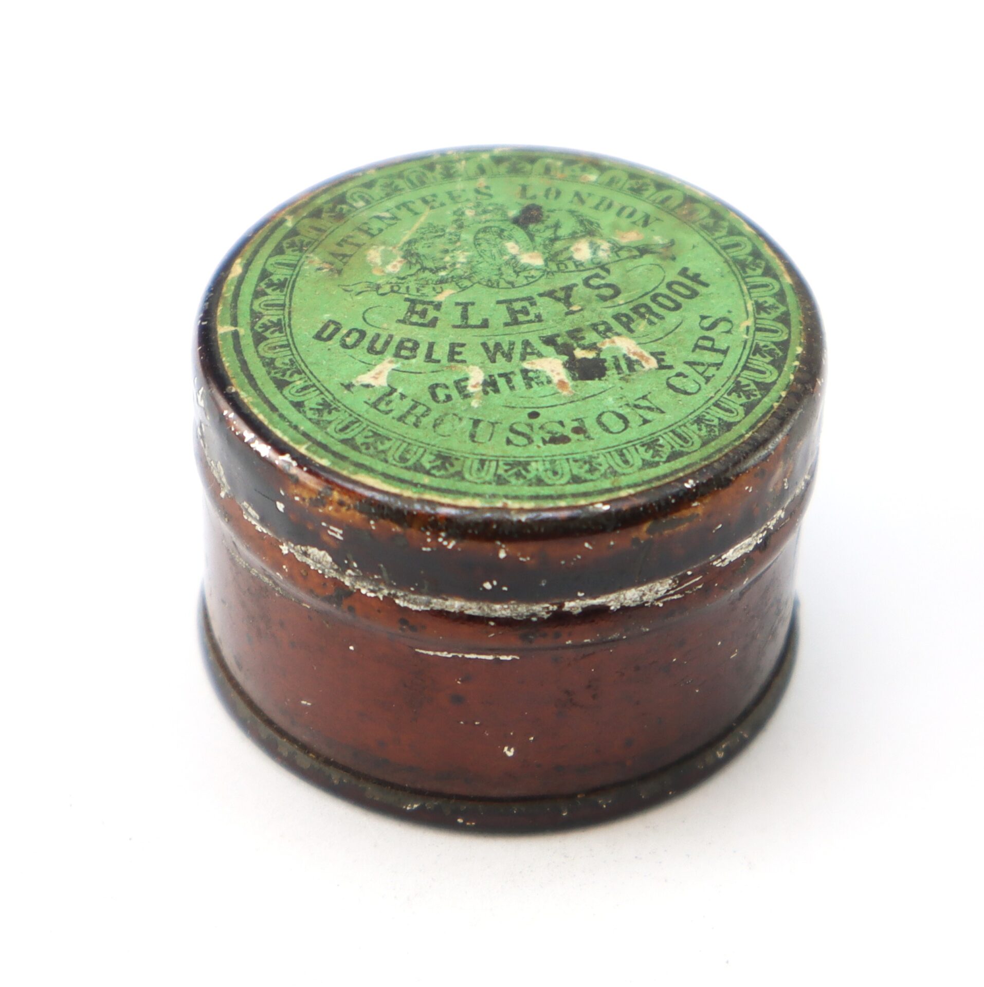 A small round tin container with a green lid labeled "Eley's Double Waterproof Central Fire Percussion Caps," showing signs of age and wear.