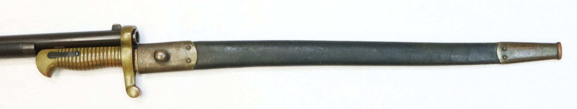 A bayonet with a brass hilt and a ribbed handle, partially sheathed in a dark scabbard with brass fittings, lying on a white background.