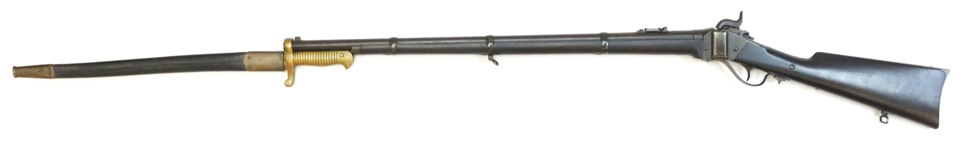 Antique single-shot rifle with a dark wood stock, metal barrel, lever action, and an attached bayonet sheathed underneath the barrel.