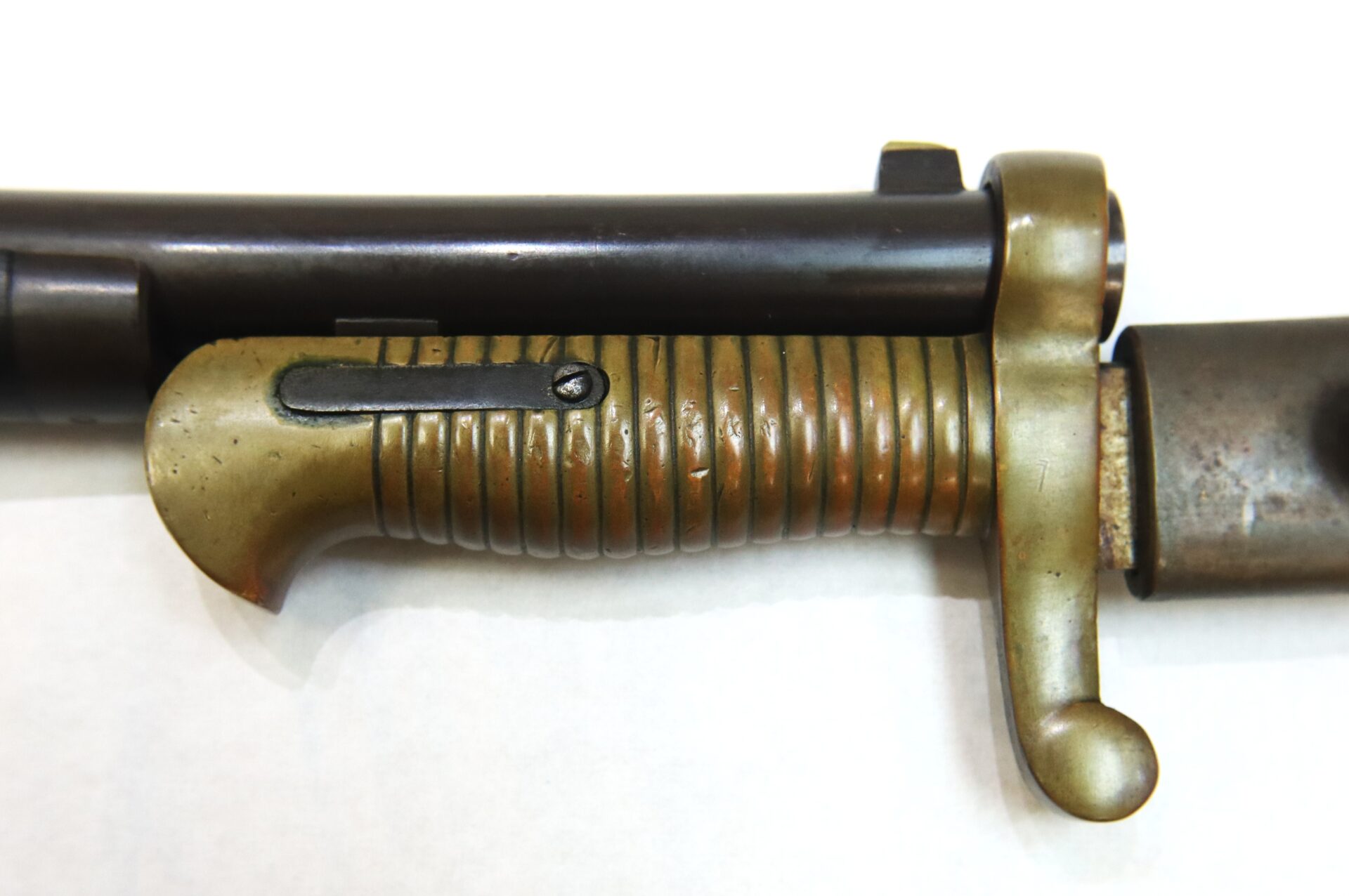 Close-up view of a rifle barrel with an attached bayonet featuring a ribbed brass handle and locking mechanism.