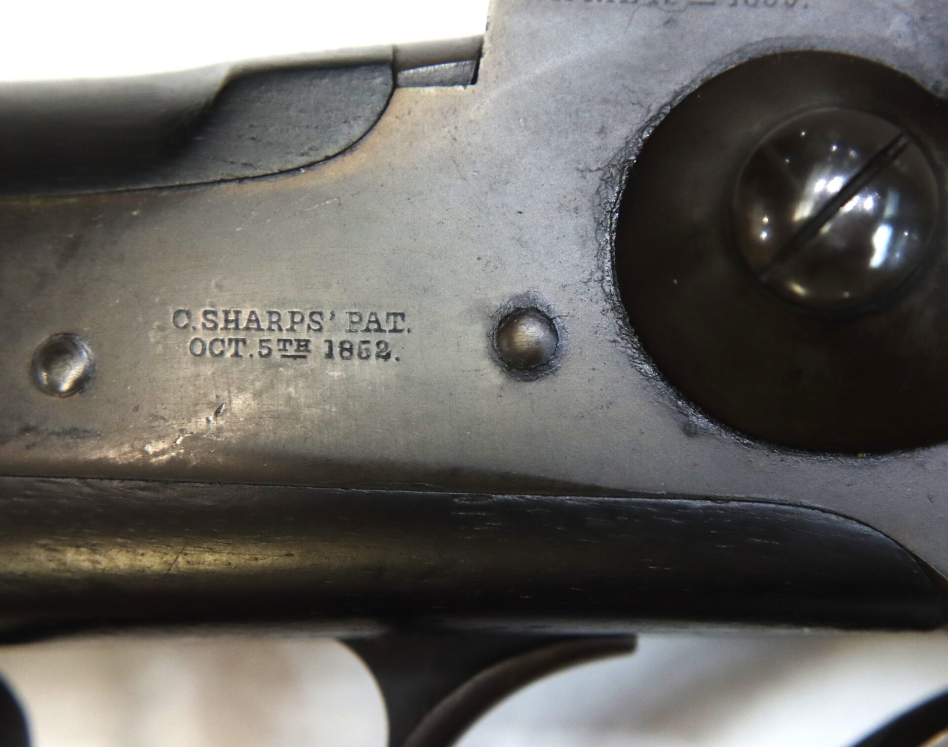 Close-up of a firearm’s metal surface showing the engraved patent mark "C. SHARPS’ PAT. OCT. 5TH 1852." and part of the trigger mechanism.