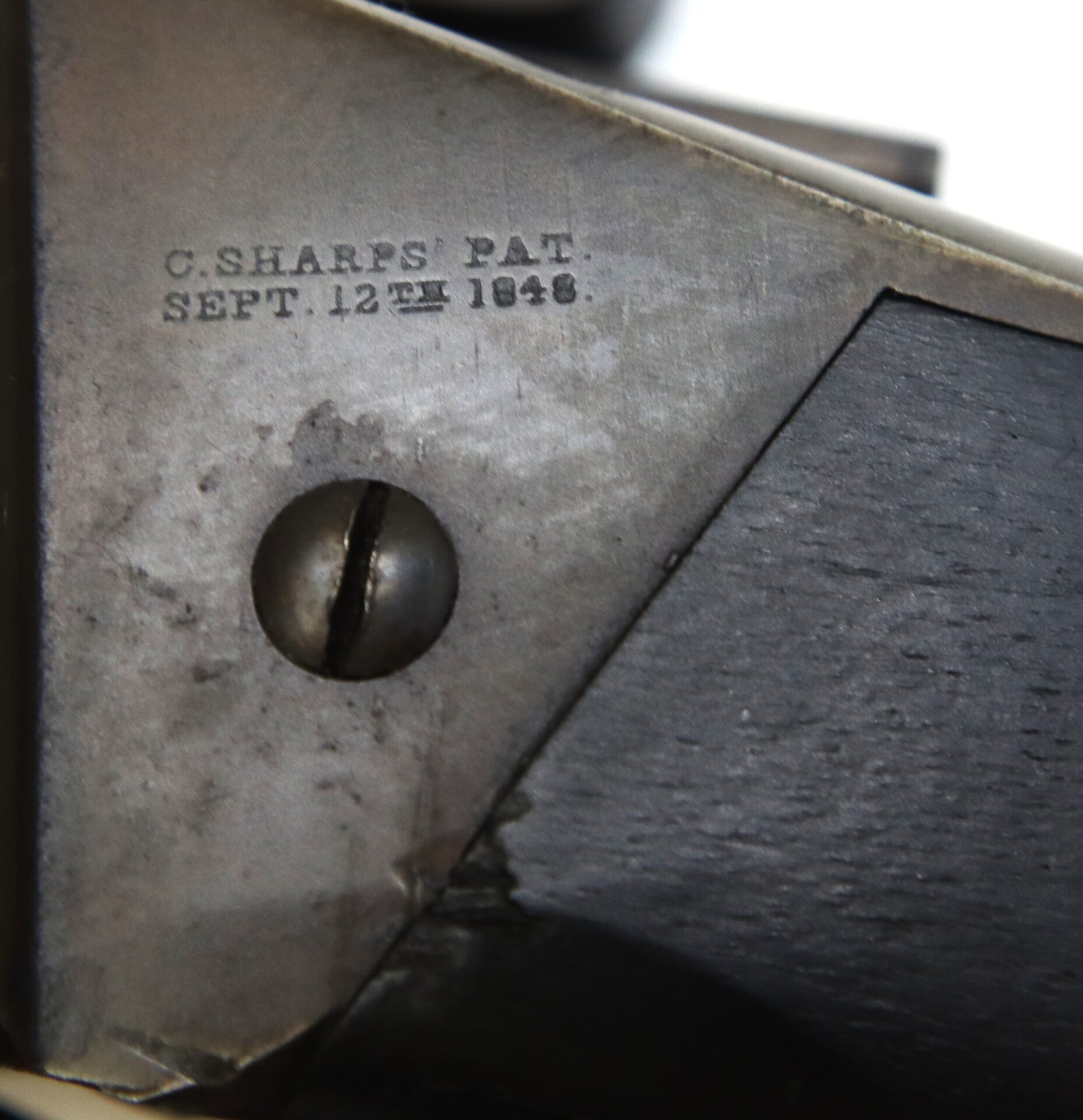 Close-up of a metal plate with an engraved inscription reading "C. SHARPS PAT. SEPT. 12TH 1848" next to a flathead screw and part of a wooden surface.