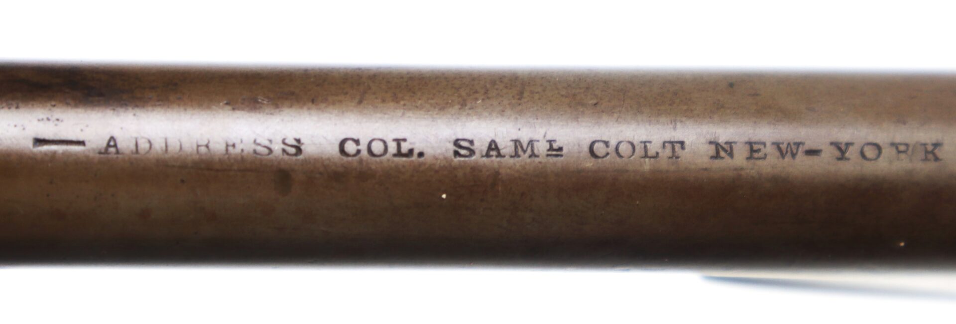 Close-up of a metal firearm barrel engraved with the text: "ADDRESS COL. SAM L COLT NEW-YORK".