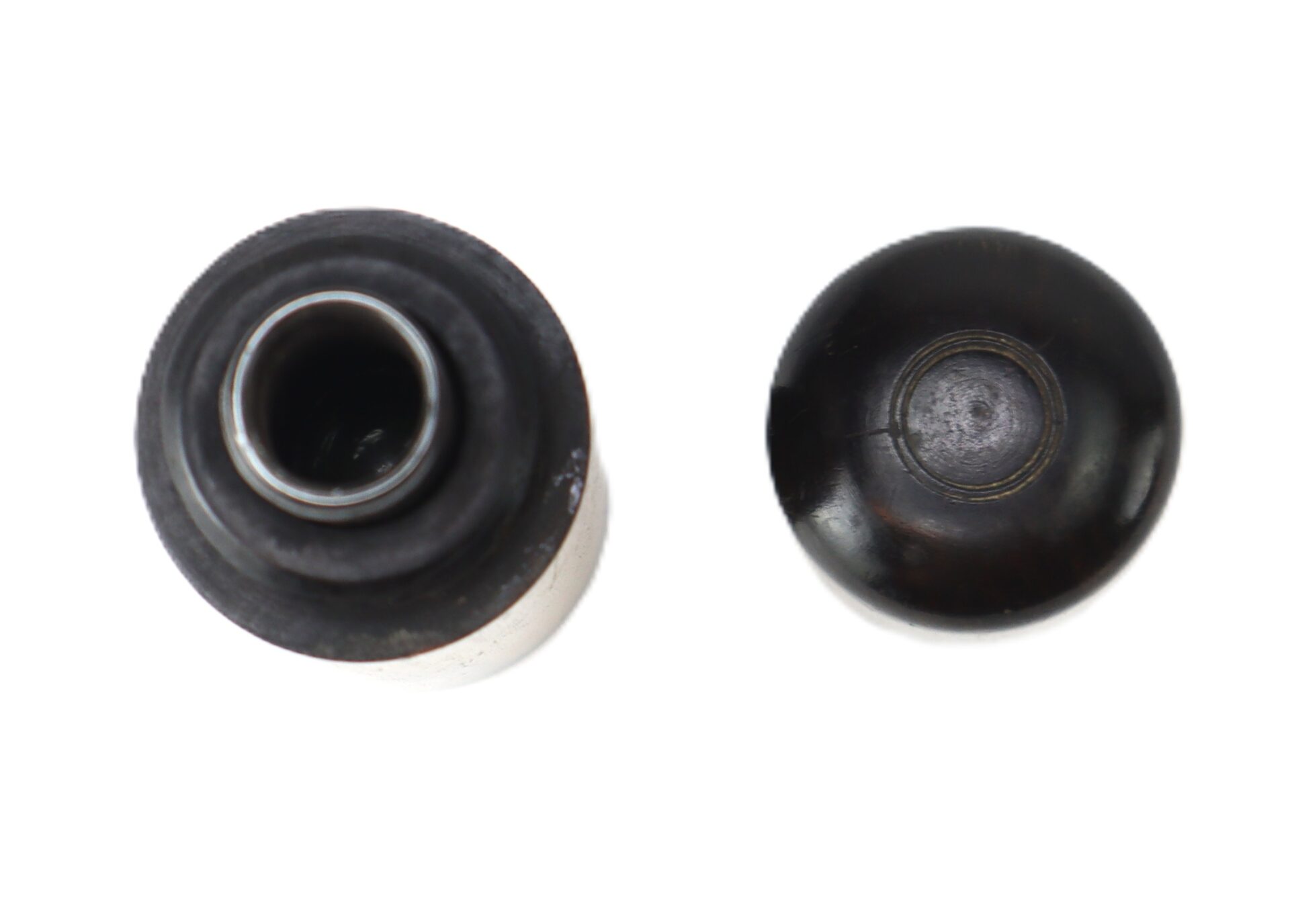 Two black circular objects on a white background, one showing an open top view with a visible metal ring, the other showing a closed, rounded surface.
