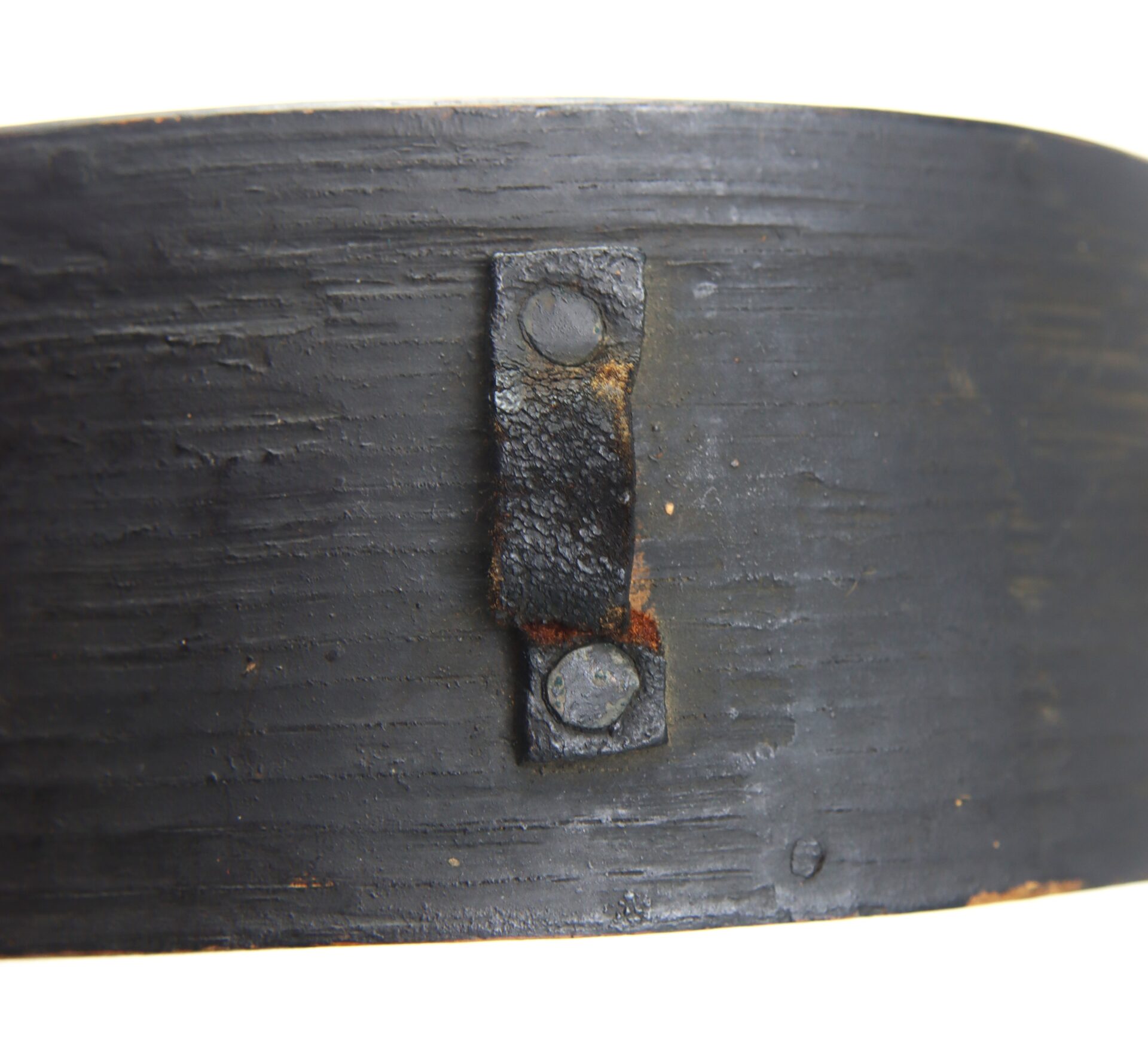 Close-up of a Mexican War Cheesebox Canteen featuring a black metal band with a small, rectangular, rusted plate attached by two rivets.