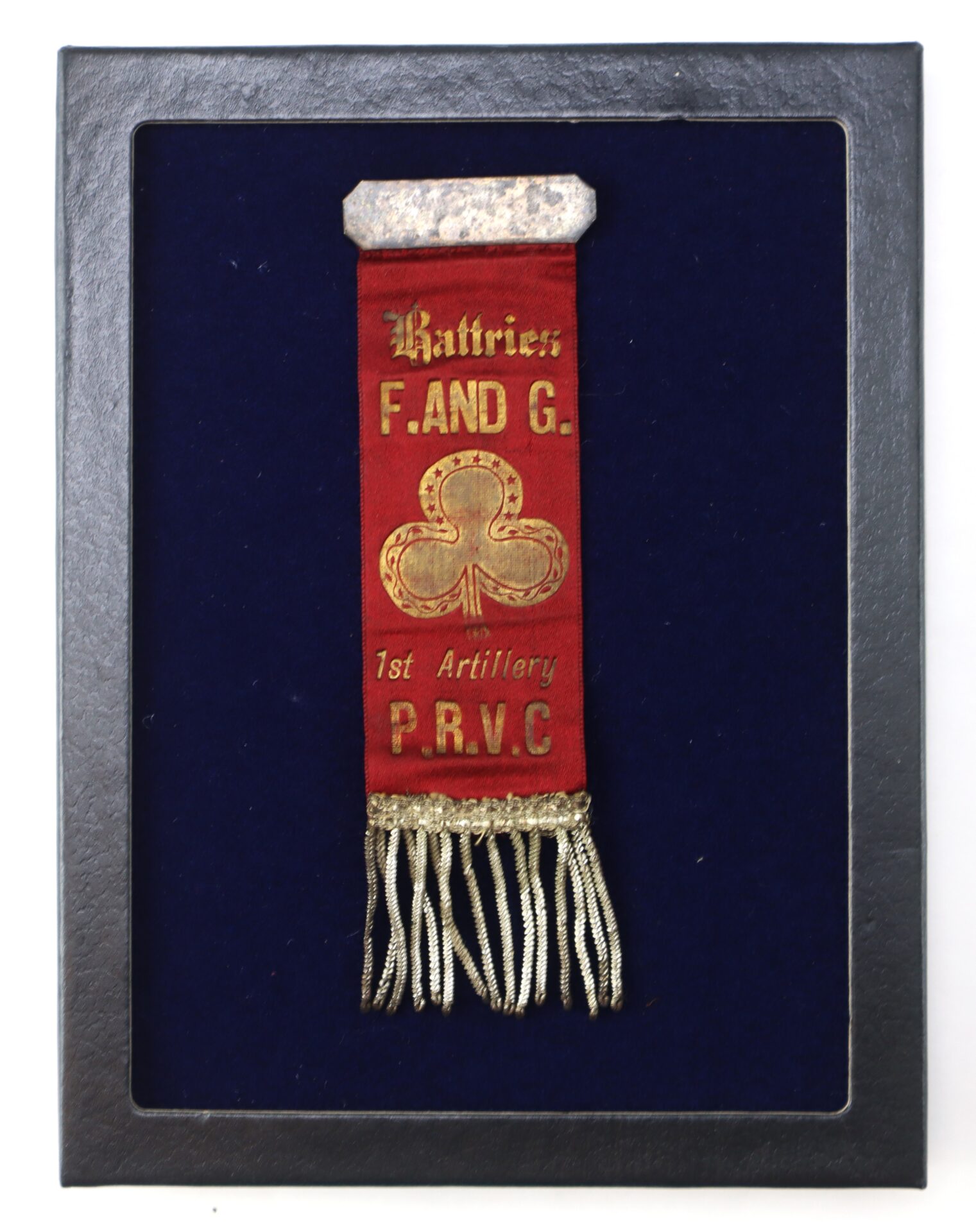 A red ribbon with gold text reading "Batteries F. AND G. 1st Artillery P.R.V.C." is framed against a dark blue background, with metallic fringe at the bottom.