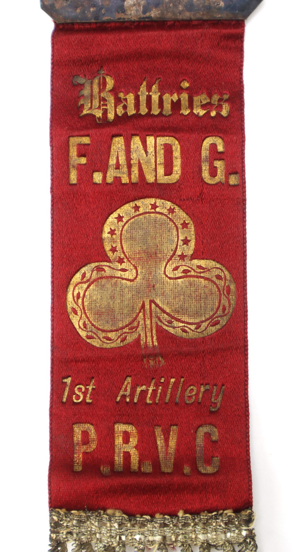 Red ribbon with gold text reading “Batteries F. AND G. 1st Artillery P.R.V.C.” and a gold clover emblem with stars, with decorative trim at the bottom.