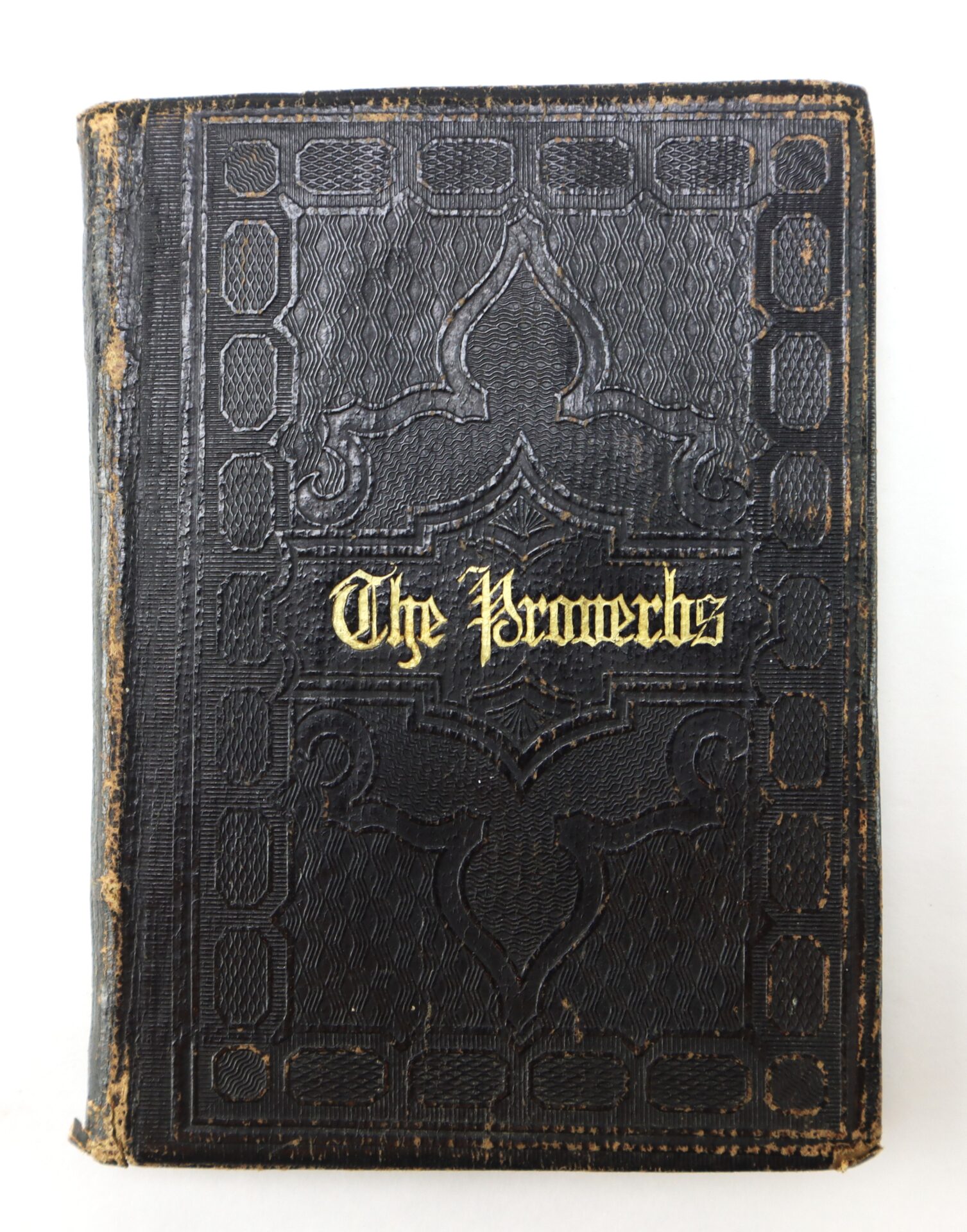 A worn, black leather-bound book with ornate patterns and the title "The Proverbs" embossed in gold lettering on the cover.