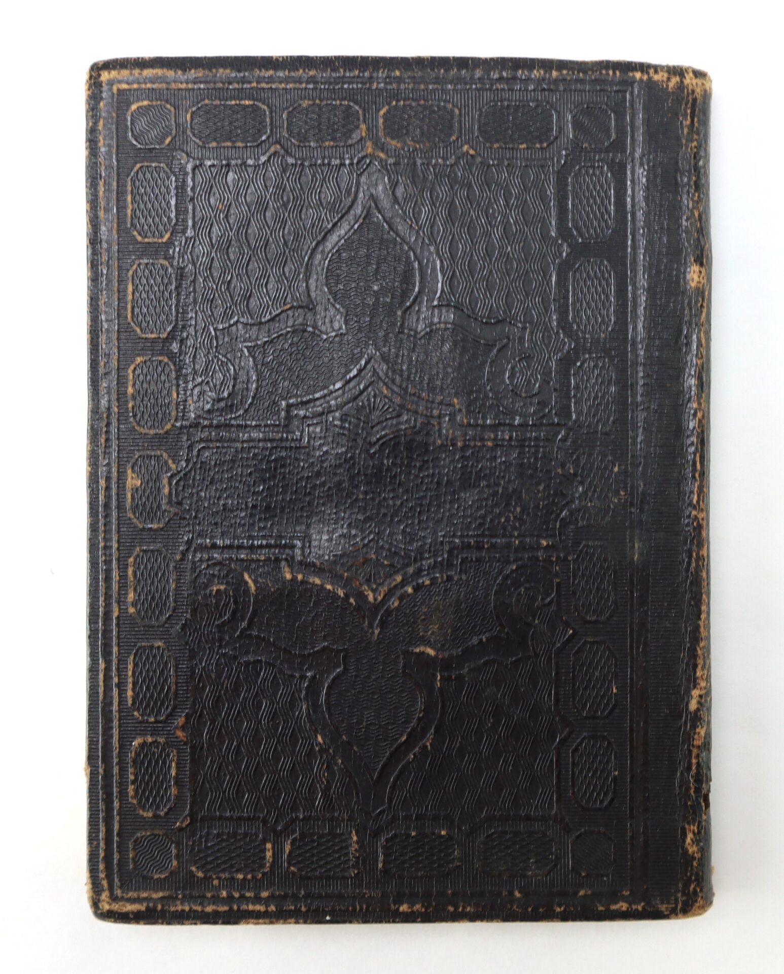A worn, embossed black leather book cover with decorative patterns, viewed from above against a white background.