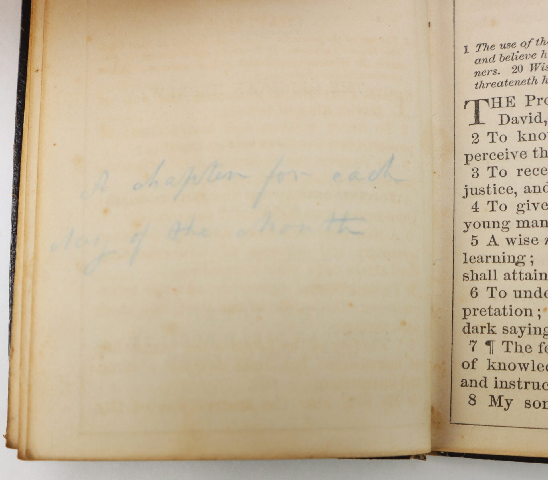 An old book open to a page with faint handwriting that reads, "1 chapter for each day of the month." Text from another page is partially visible on the right.