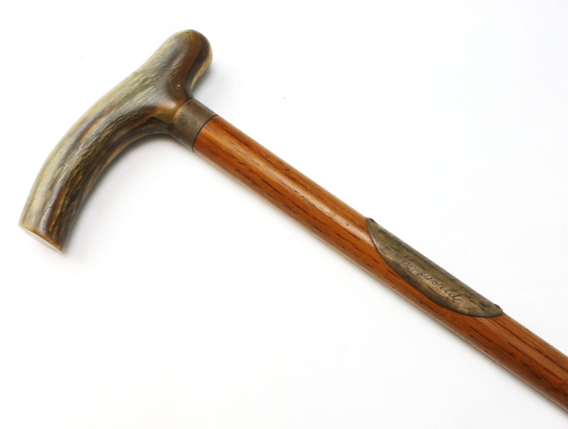 A wooden cane with a curved handle and a metal plate inset near the top, photographed on a white background.