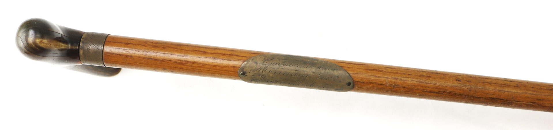 A wooden cane with a curved dark handle and a metal plaque attached near the top engraved with text.