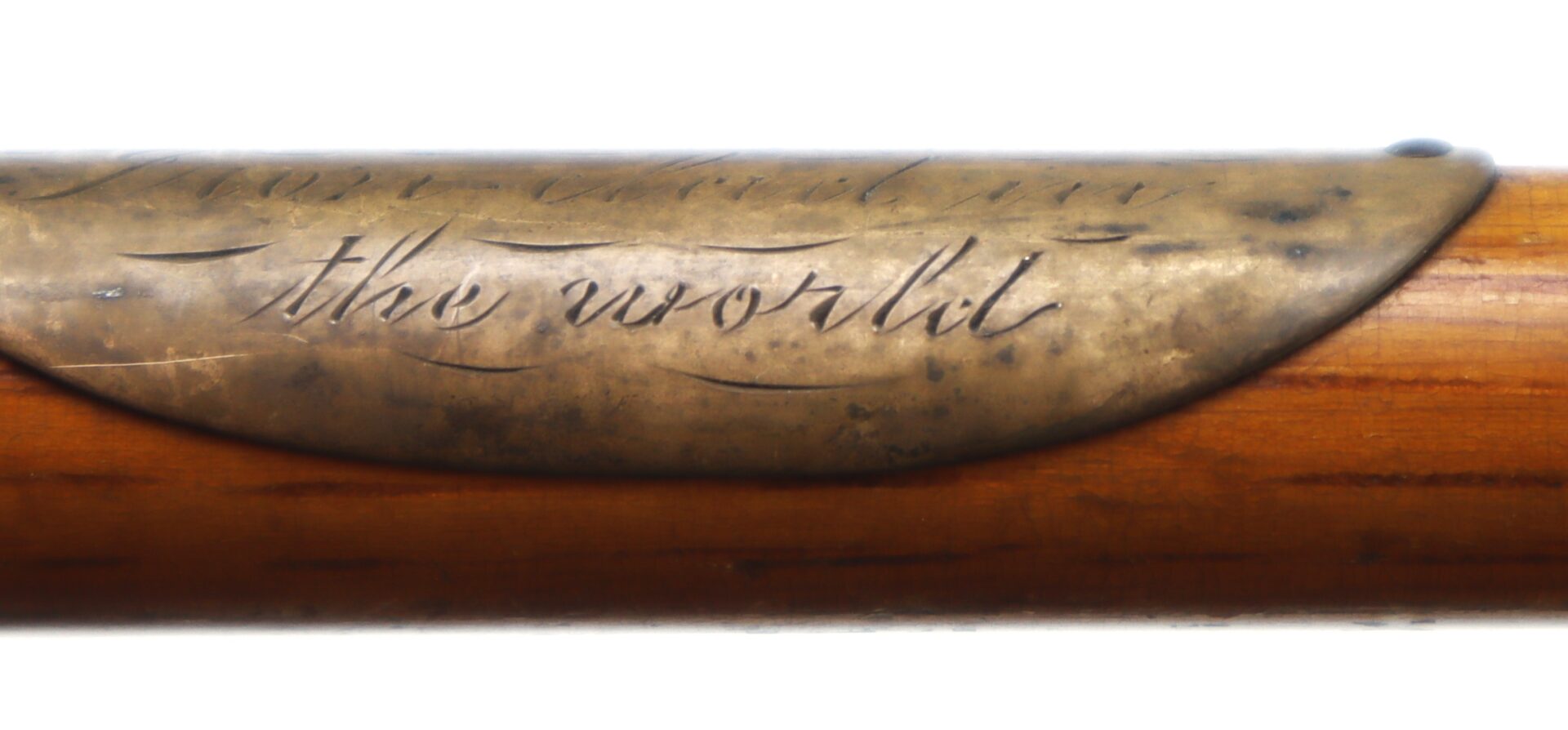 Close-up of an engraved metal plate on a wooden surface, displaying the words "the world" in cursive script.