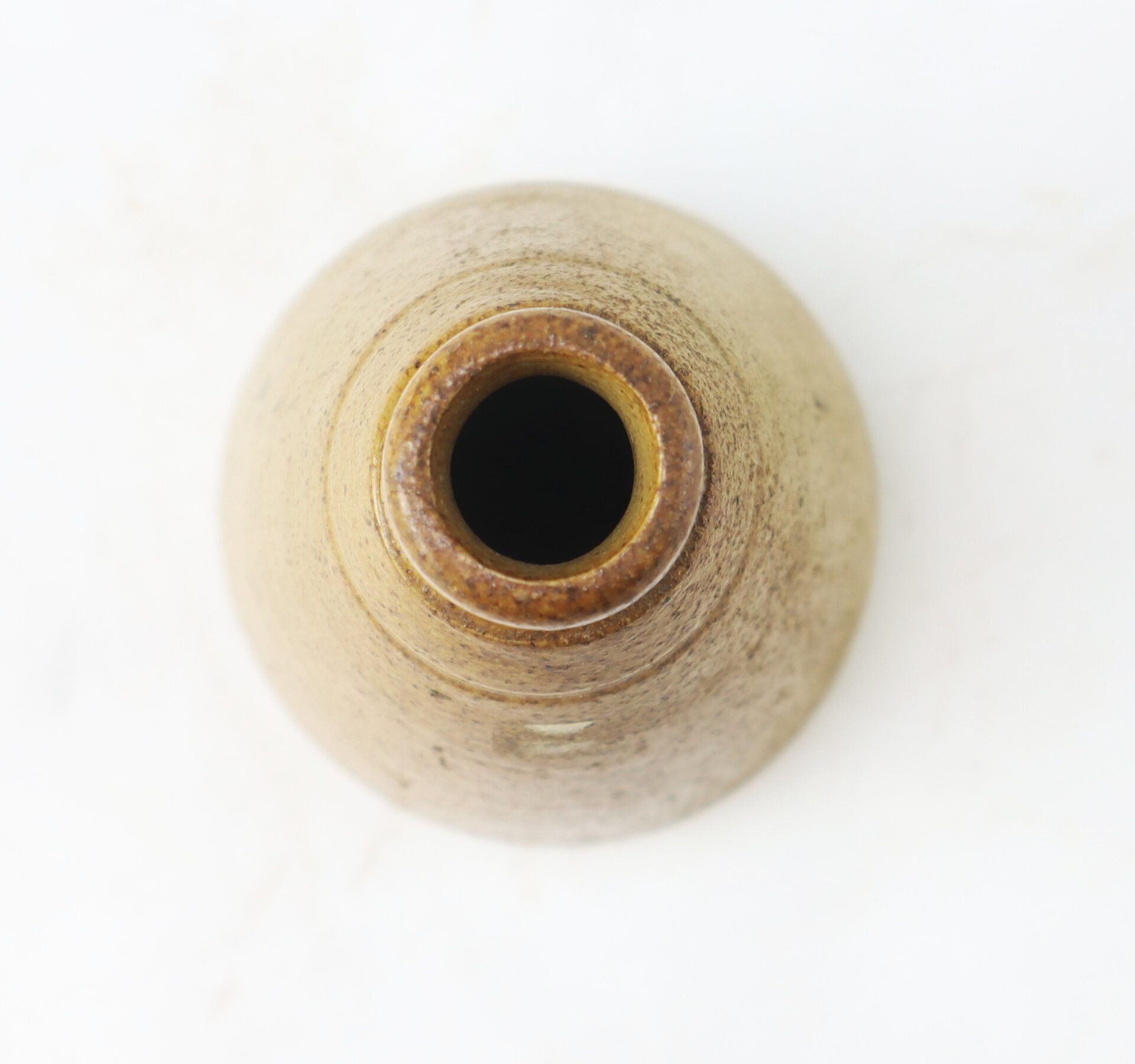 Top view of a small, round, brown ceramic vase with a narrow opening, placed on a white surface.