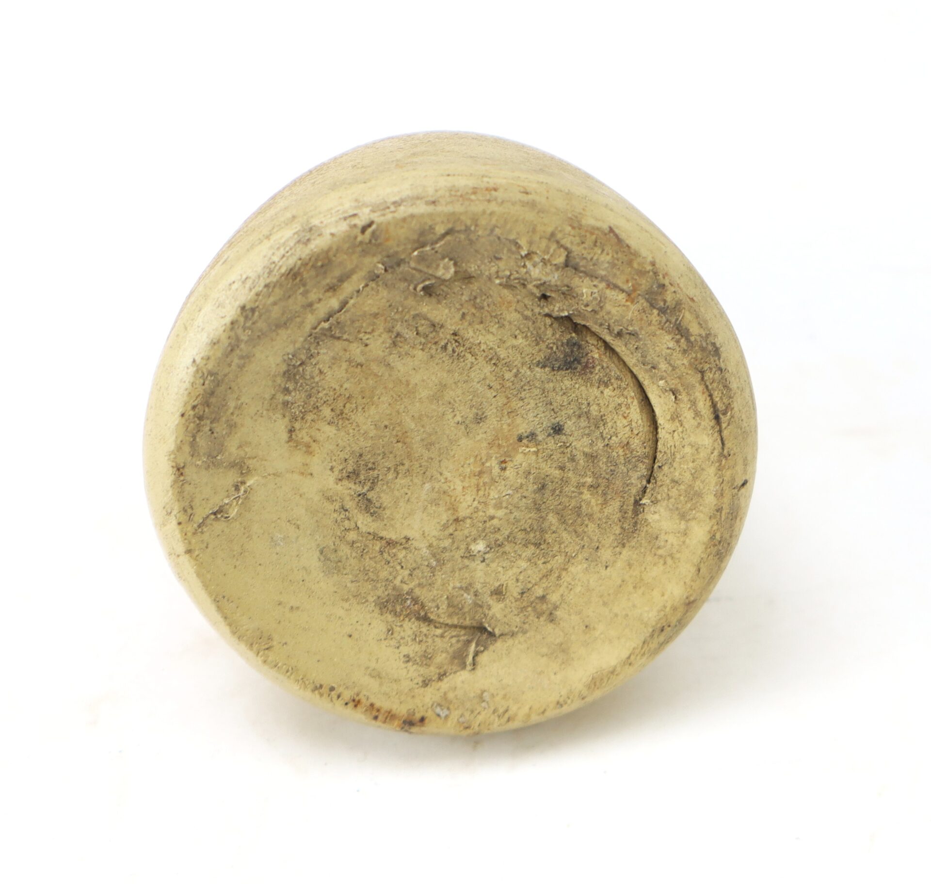 A close-up view of the base of a round, worn, and tarnished metal object on a white background.