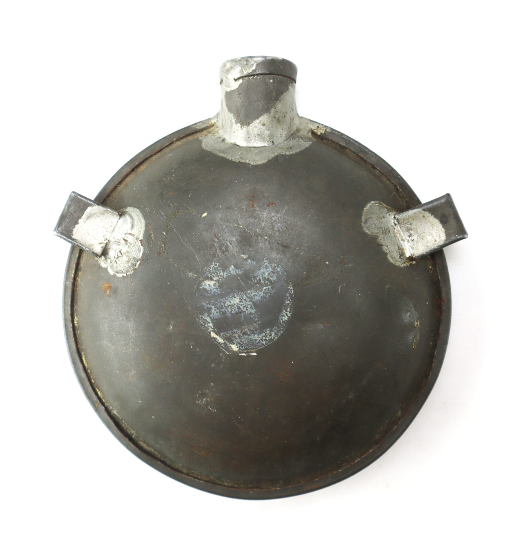 A round, metal canteen with three spouts or handles, showing signs of wear and a faded marking on its surface.