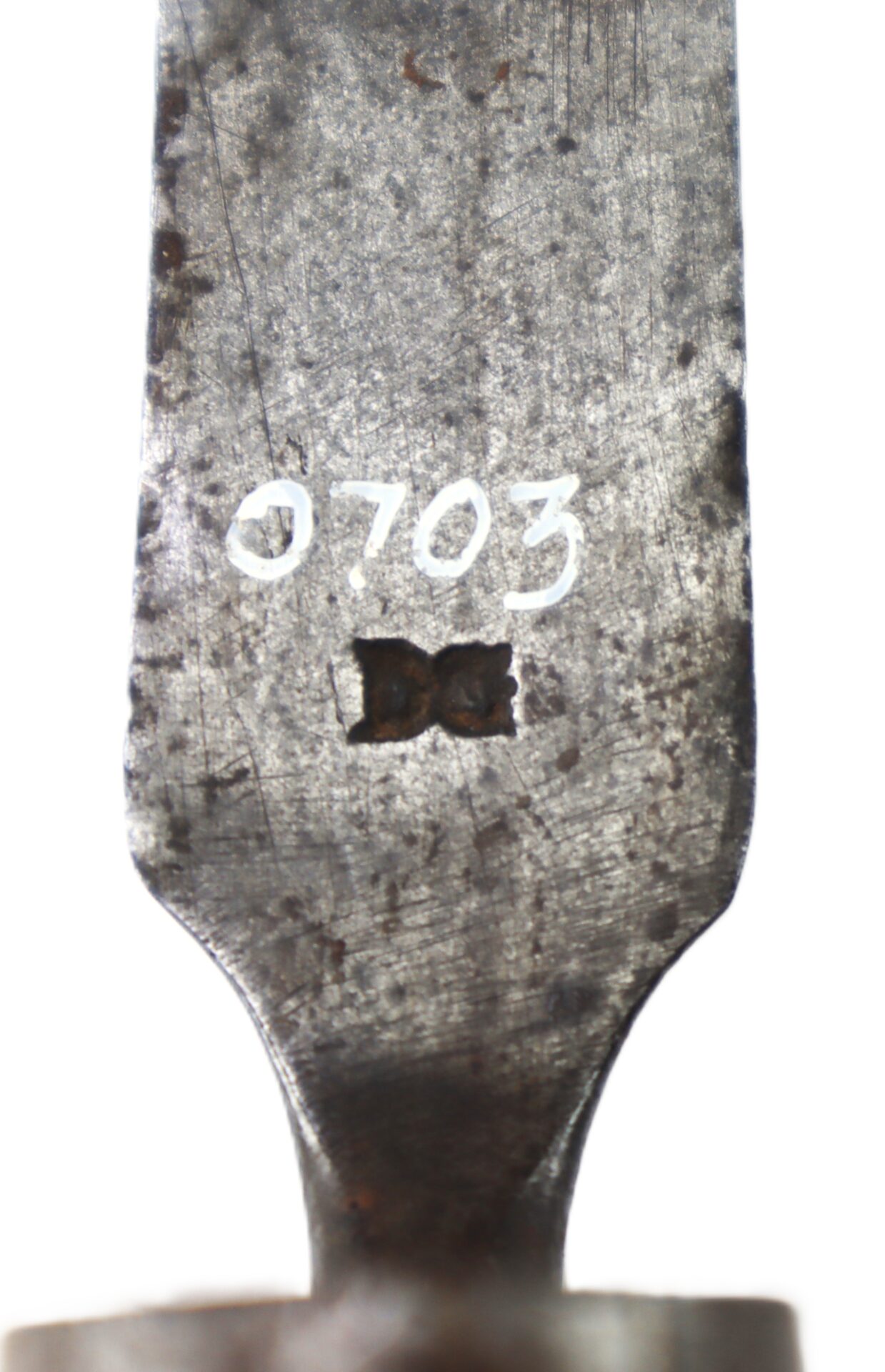 Close-up of a metal surface with the number "0703" and a small, bow-tie shaped marking engraved on it.