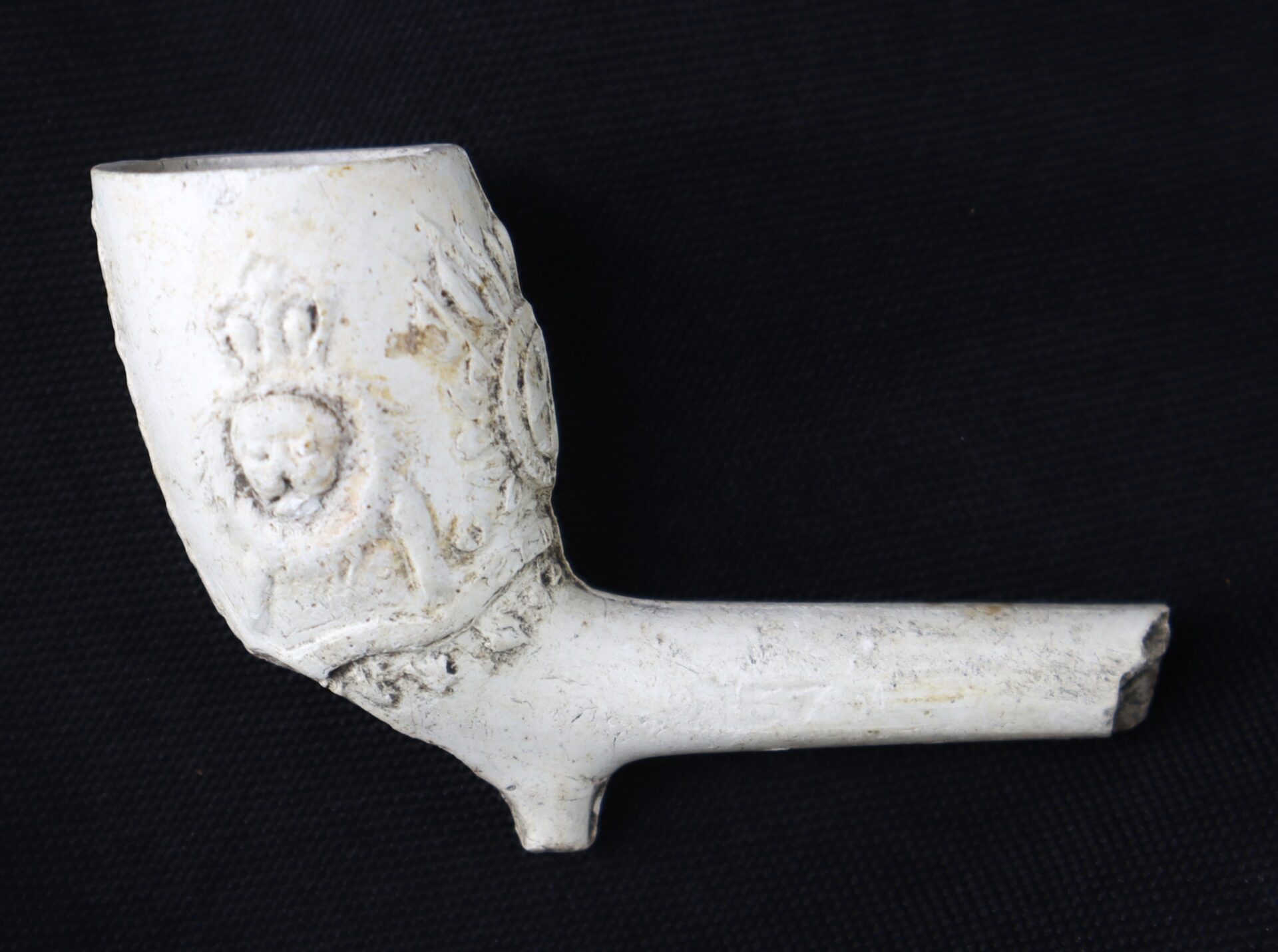 A white clay tobacco pipe with a short stem and embossed lion and crown design on the bowl, displayed against a black background.