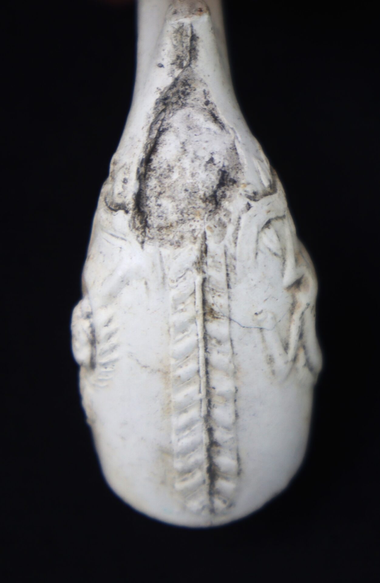Close-up view of an old, white clay pipe bowl with a braided or rope-like raised design and visible surface wear.