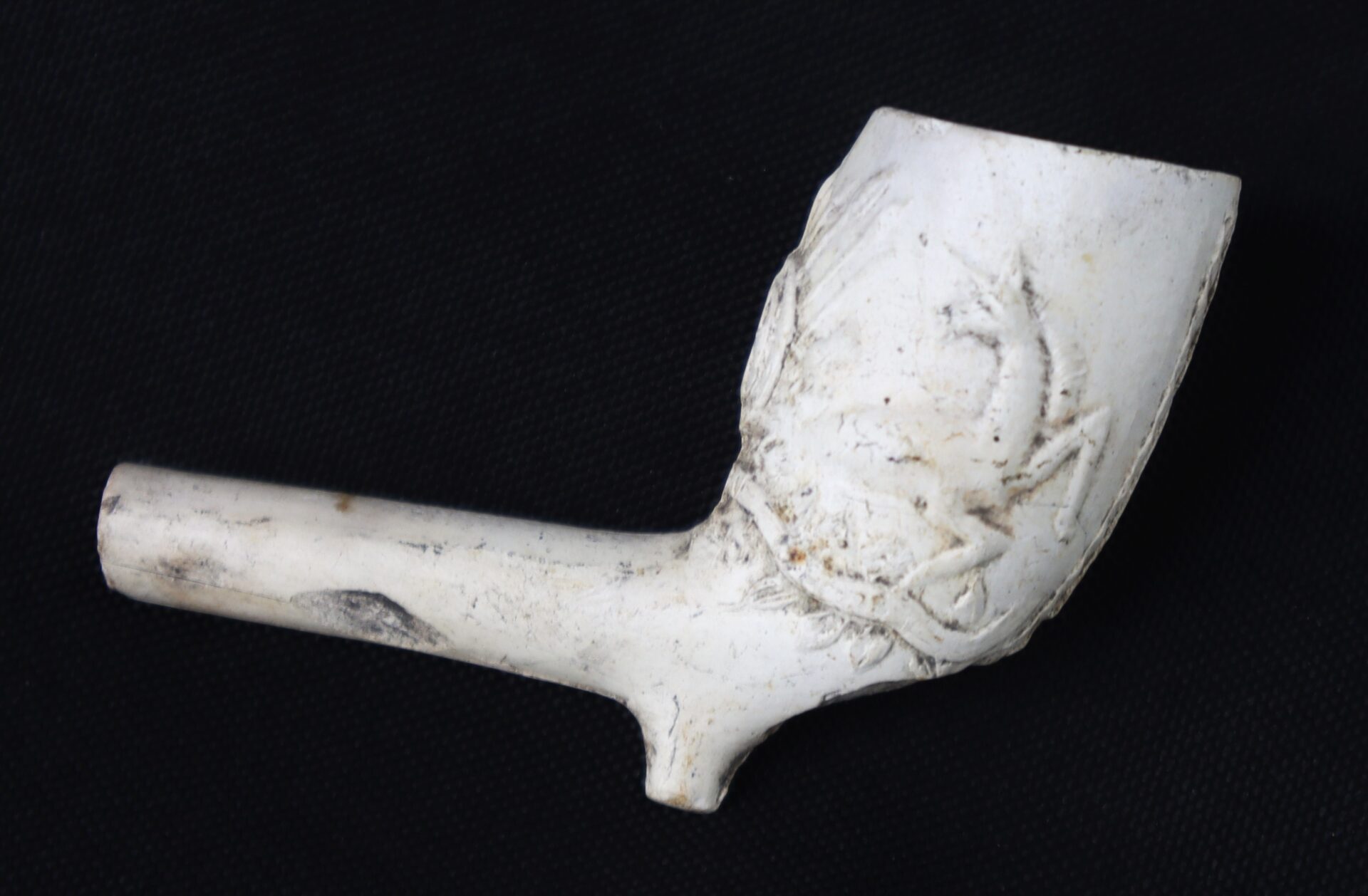 A white clay tobacco pipe with an engraved decorative pattern, shown against a black background.