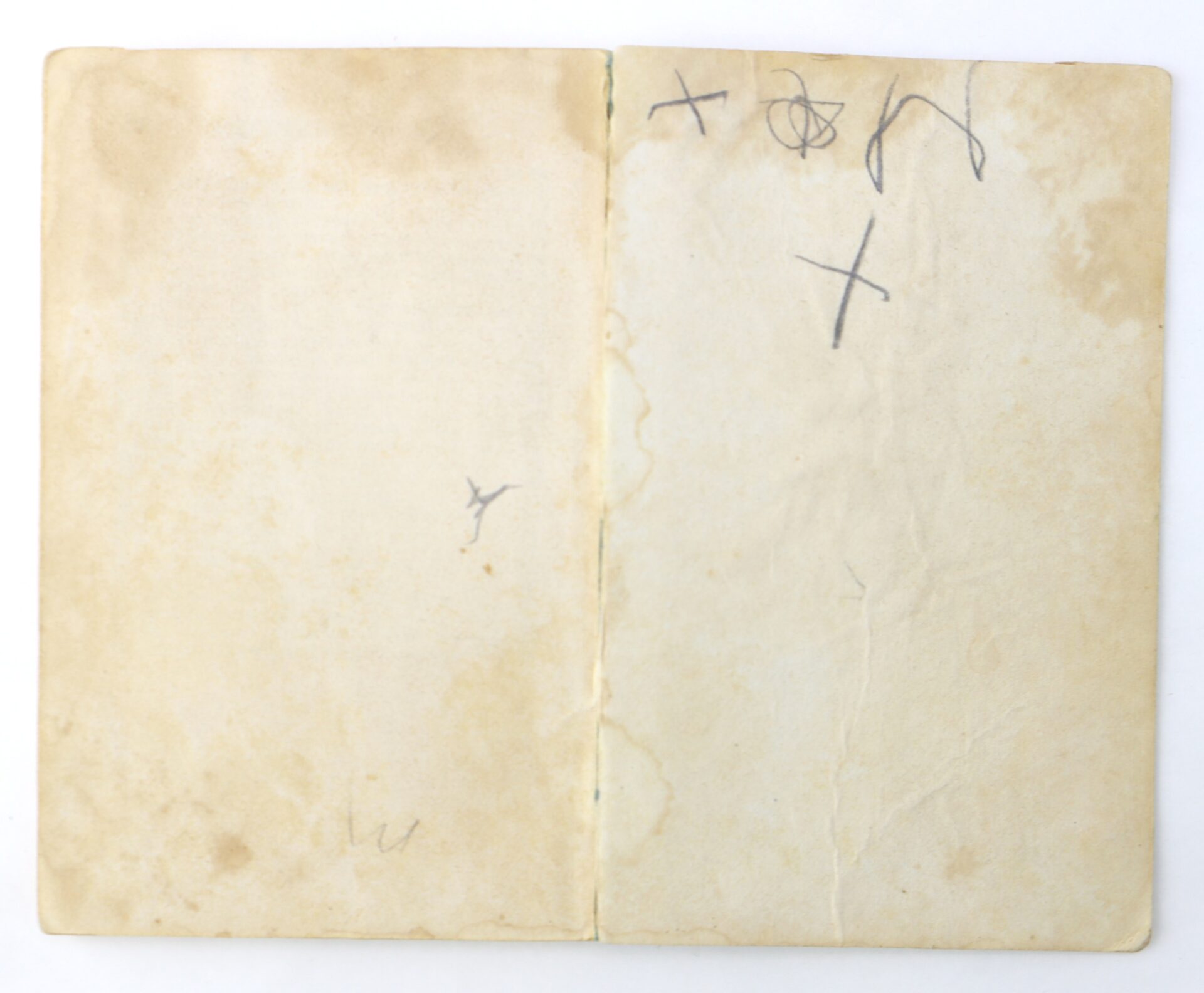 An open, aged notebook with yellowed pages, some faint stains, and a few random black scribbles and marks.