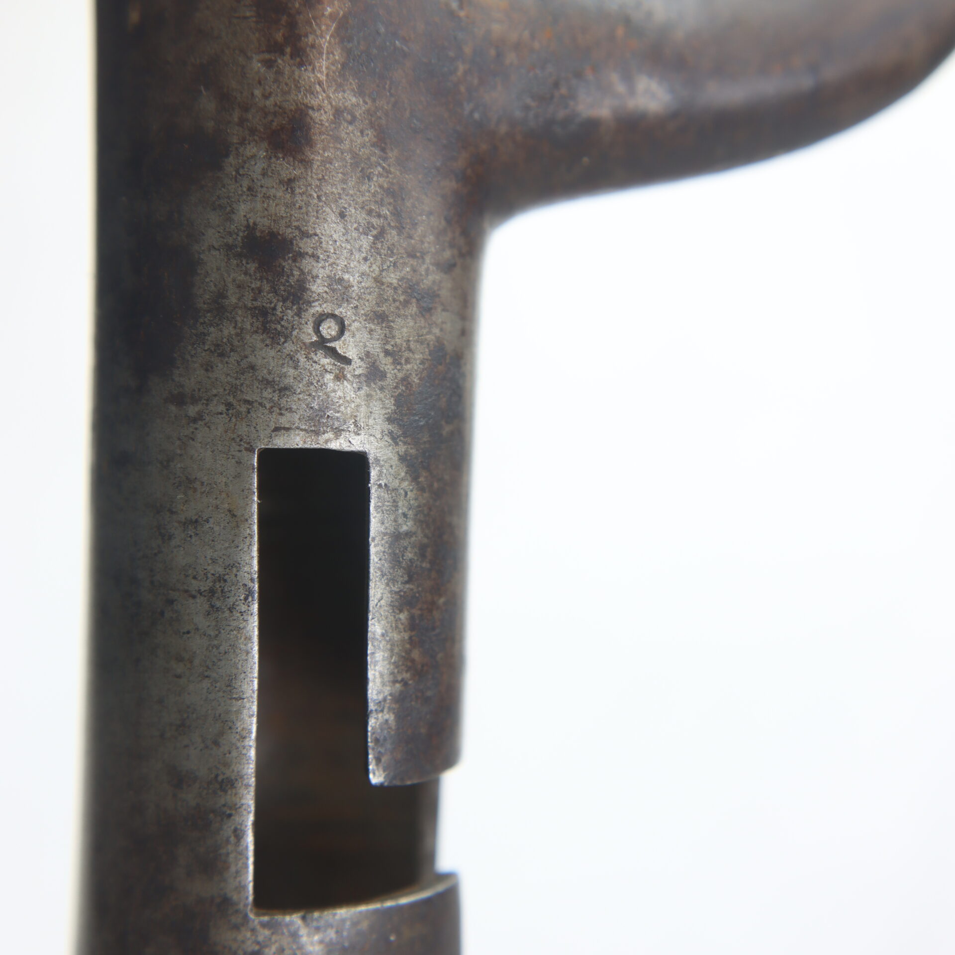Close-up of a rusted metal object with a rectangular cutout and a small stamped "Q" marking above the cutout.