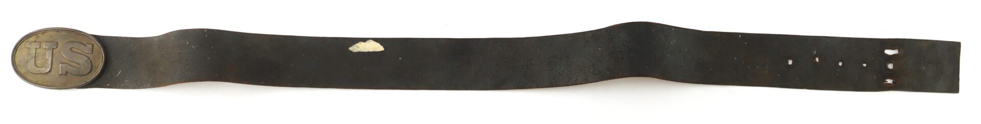 A worn leather belt with a round brass “US” buckle and several small holes and a light-colored mark along its length.