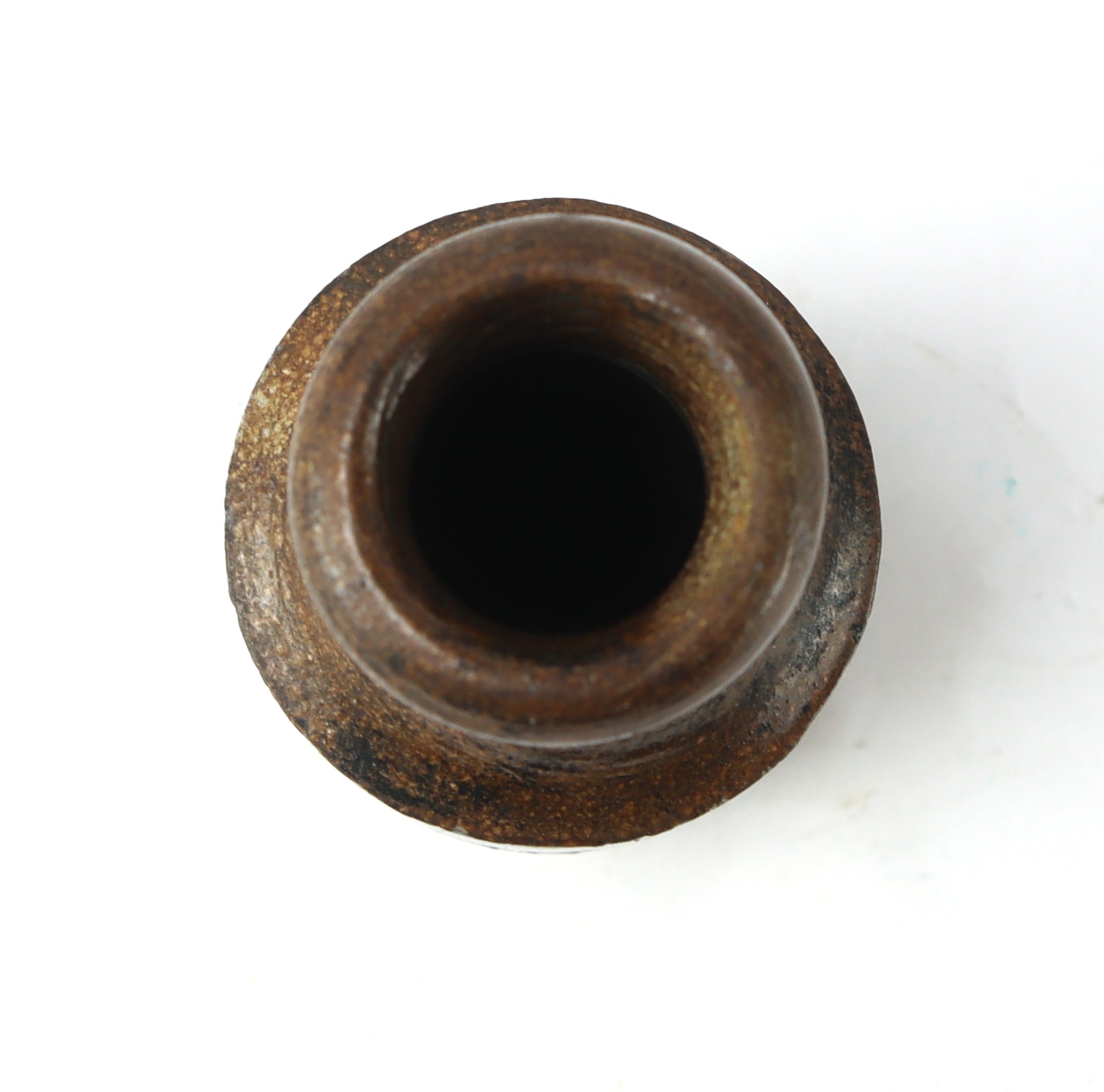 Top view of a small, round, rusted metal container or bottle with a wide opening, shown against a white background.