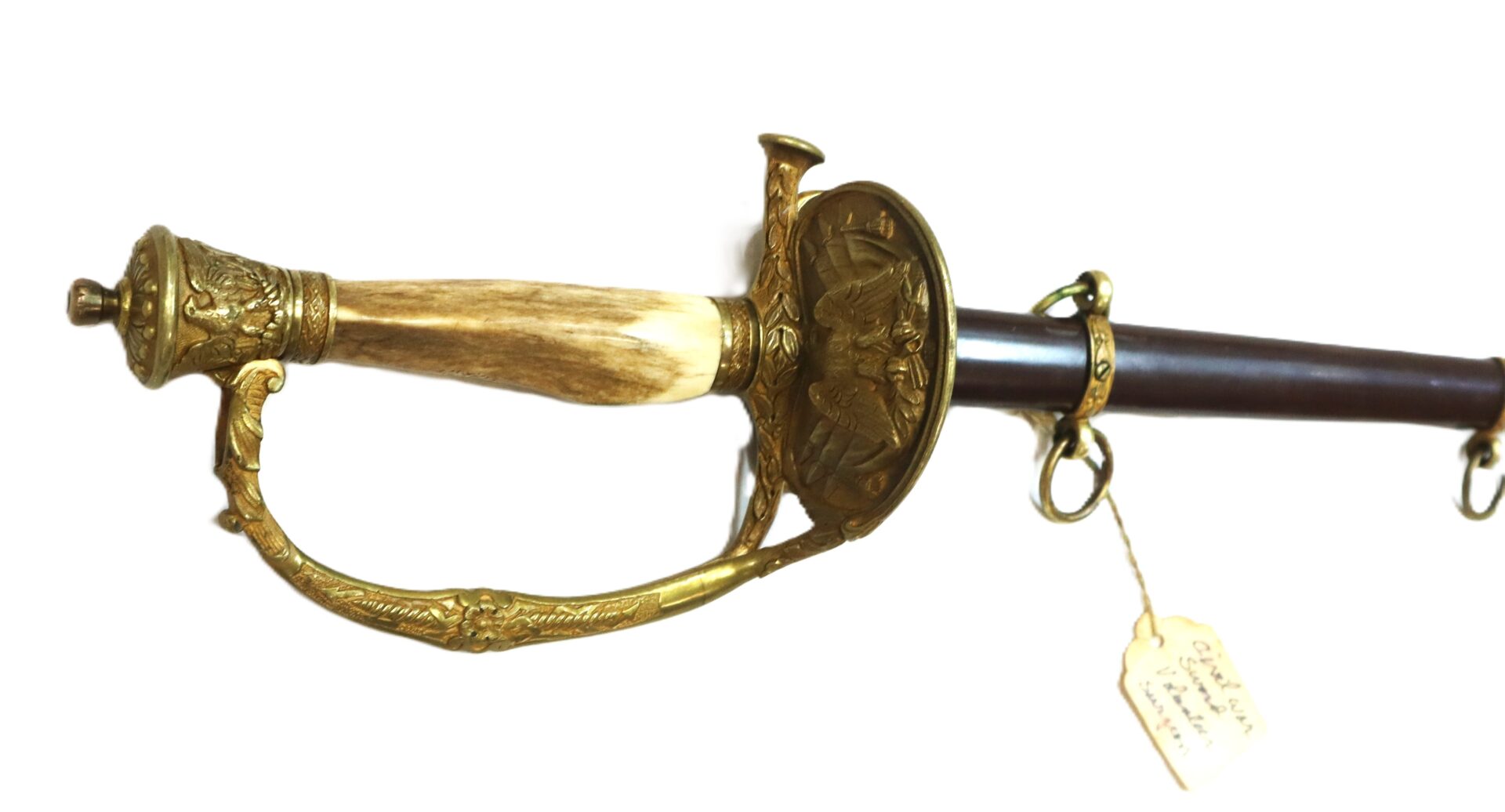 Antique sword with an ornate brass hilt, decorative guard, and a scabbard featuring metal rings and a handwritten tag.