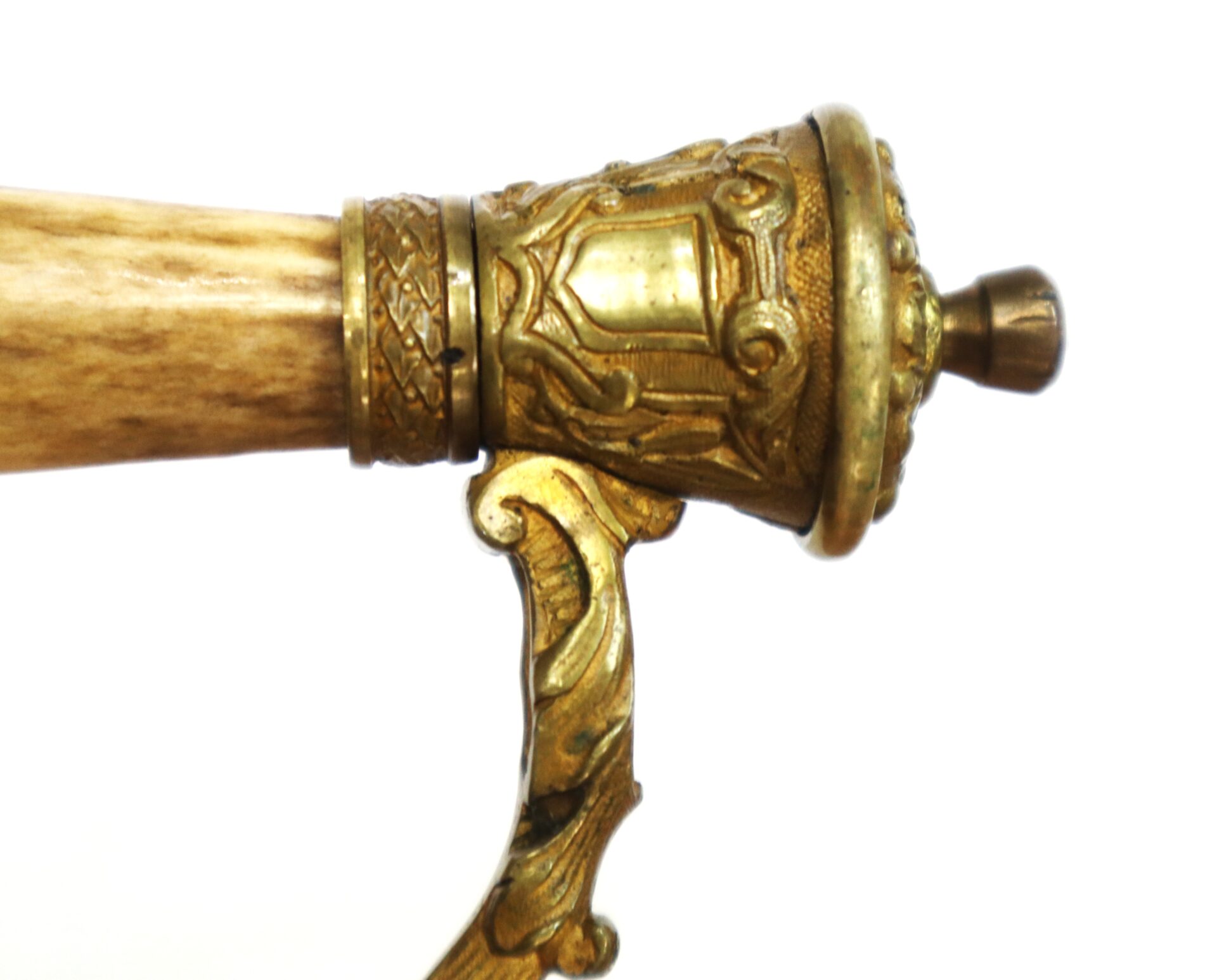 Close-up of an ornate brass and wood handle, possibly part of a ceremonial or antique sword or cane, featuring detailed engravings and decorative patterns.