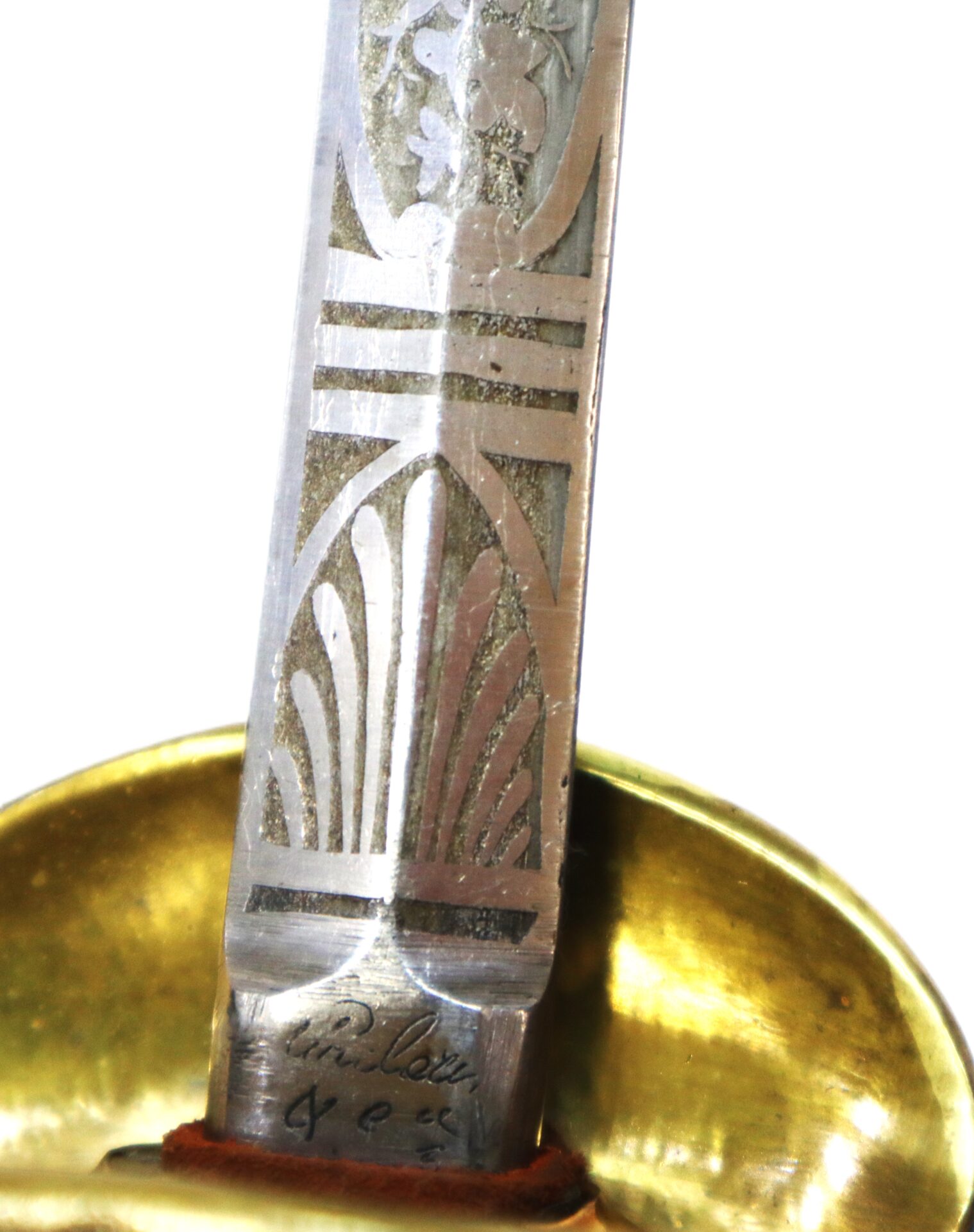 Close-up of a decorated sword blade with etched patterns and a signature near the brass guard.