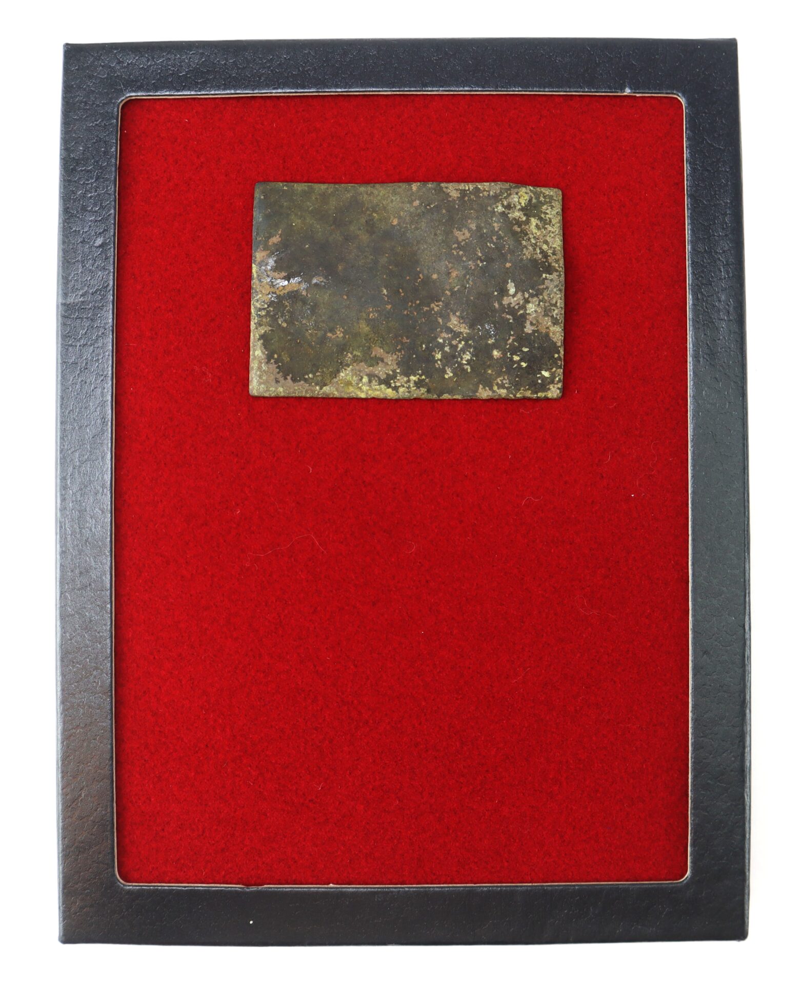 A rectangular, weathered metal object is displayed on a red felt background inside a black frame.