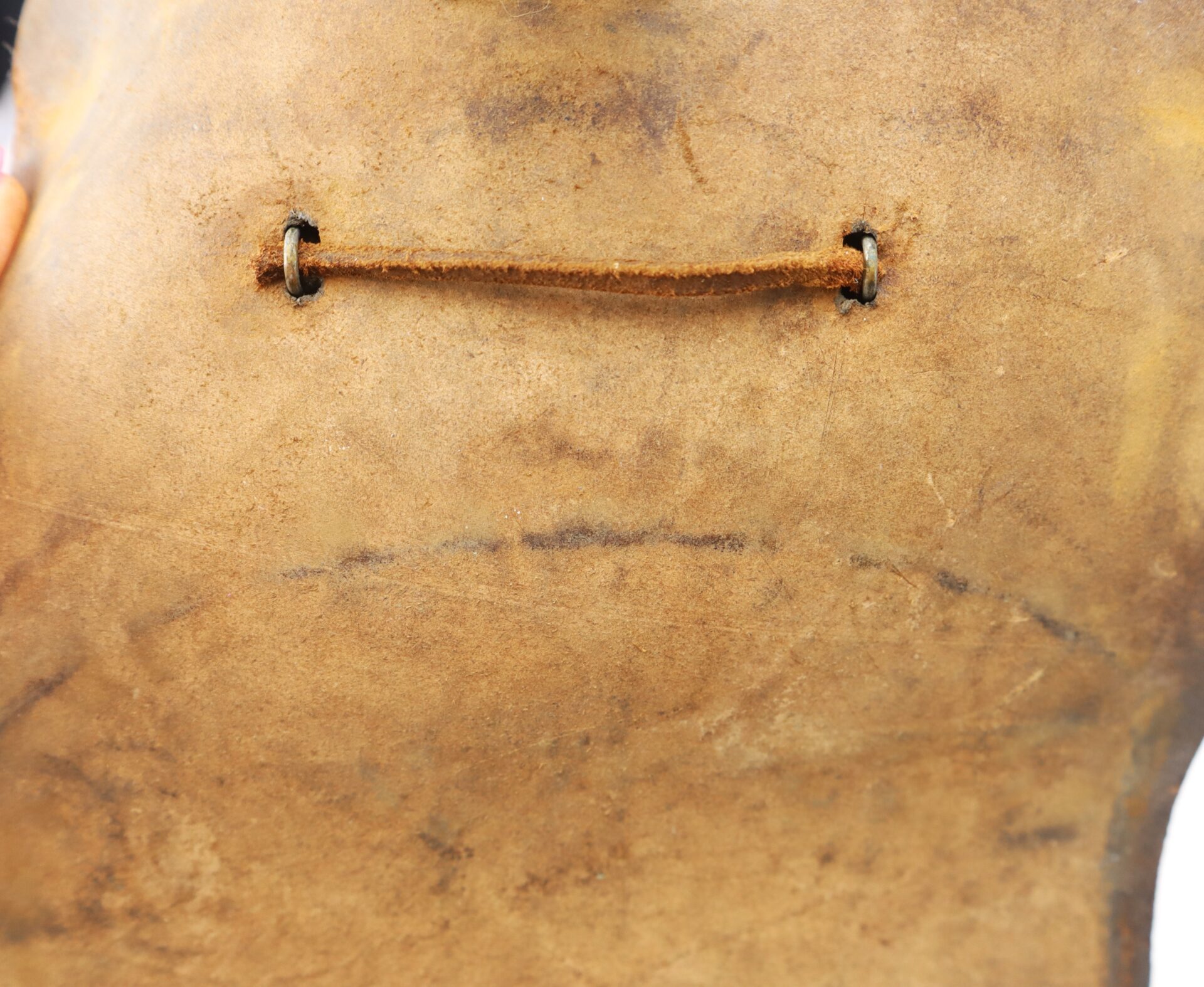 Close-up of a worn piece of brown leather with two metal-reinforced holes connected by a thin leather lace.