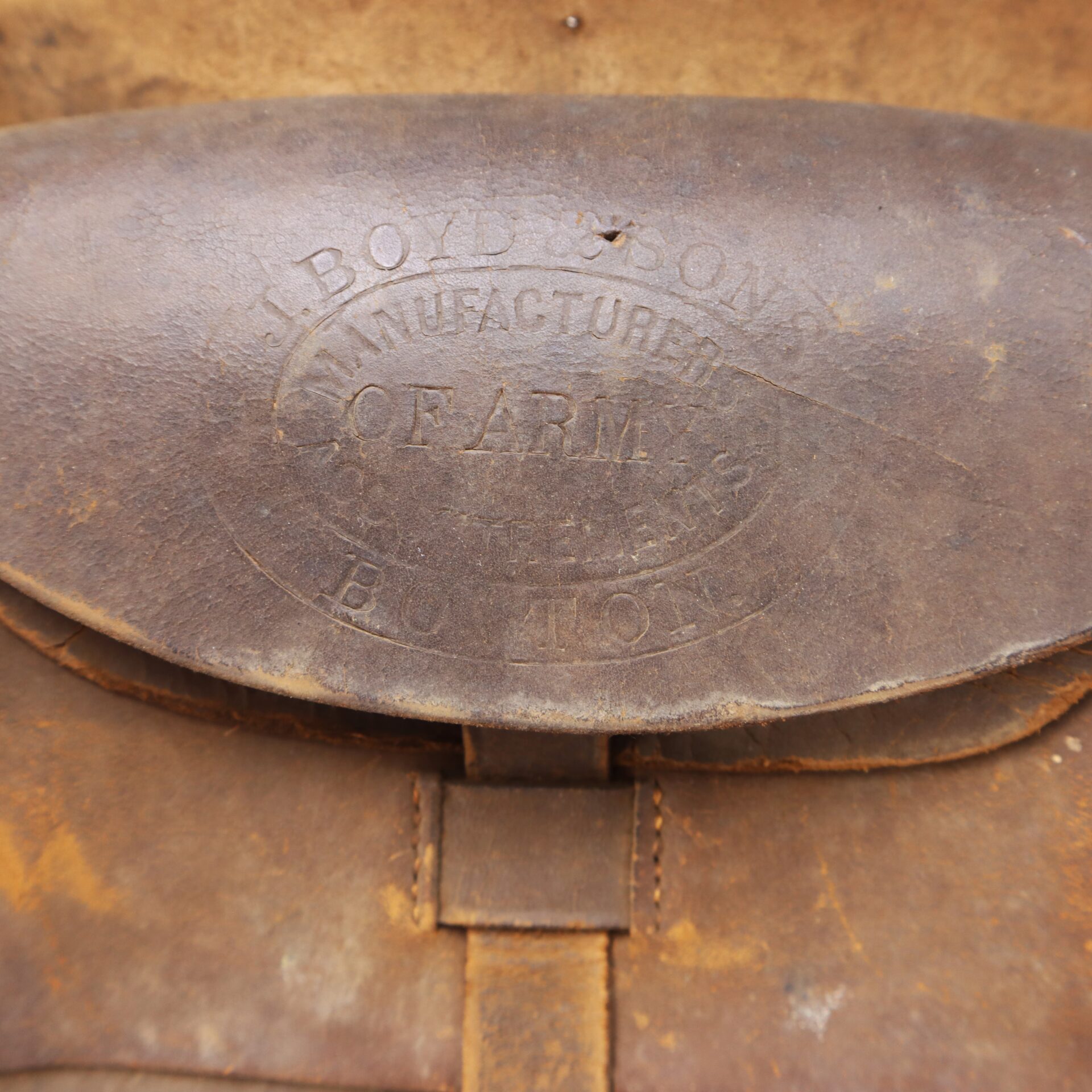 Close-up of a worn leather pouch with embossed text reading "J. Boyd & Sons, Manufactured of Arms, Boston." The leather appears aged and weathered.